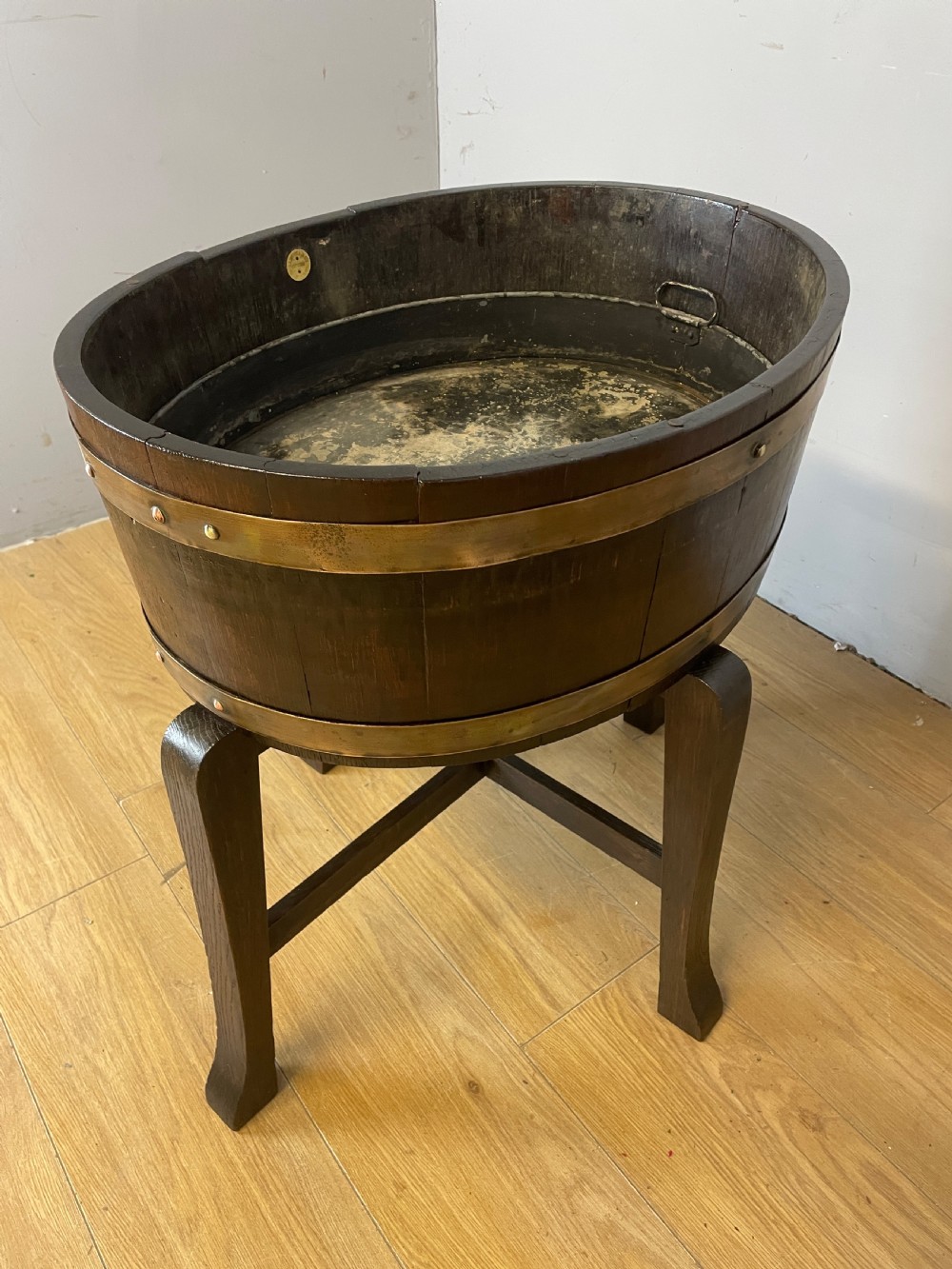An Edwardian dark oak coopered circular planter with polished brass binding bands, raised on a three-legged wooden stand. View VI