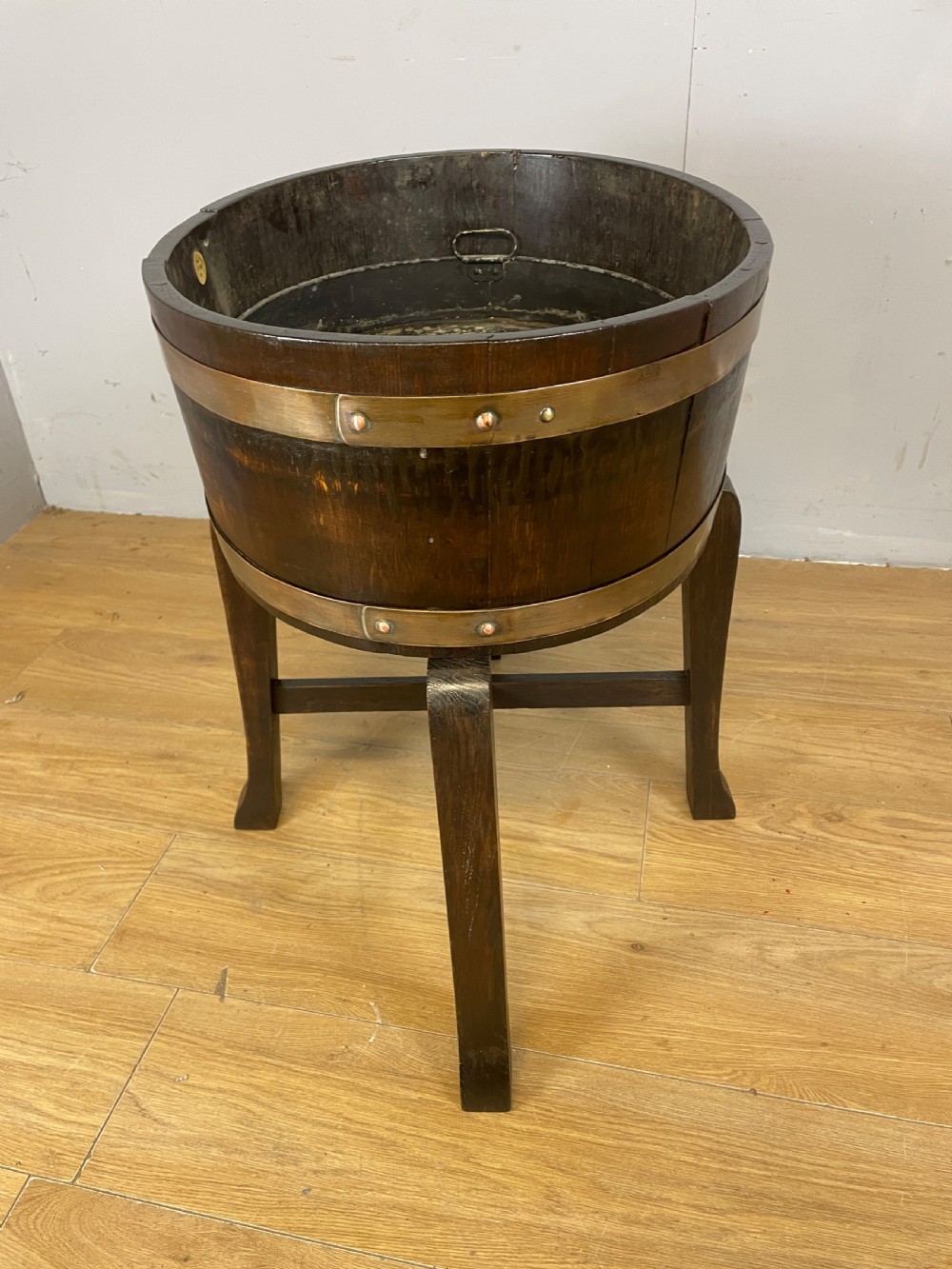 An Edwardian dark oak coopered circular planter with polished brass binding bands, raised on a three-legged wooden stand. View VII