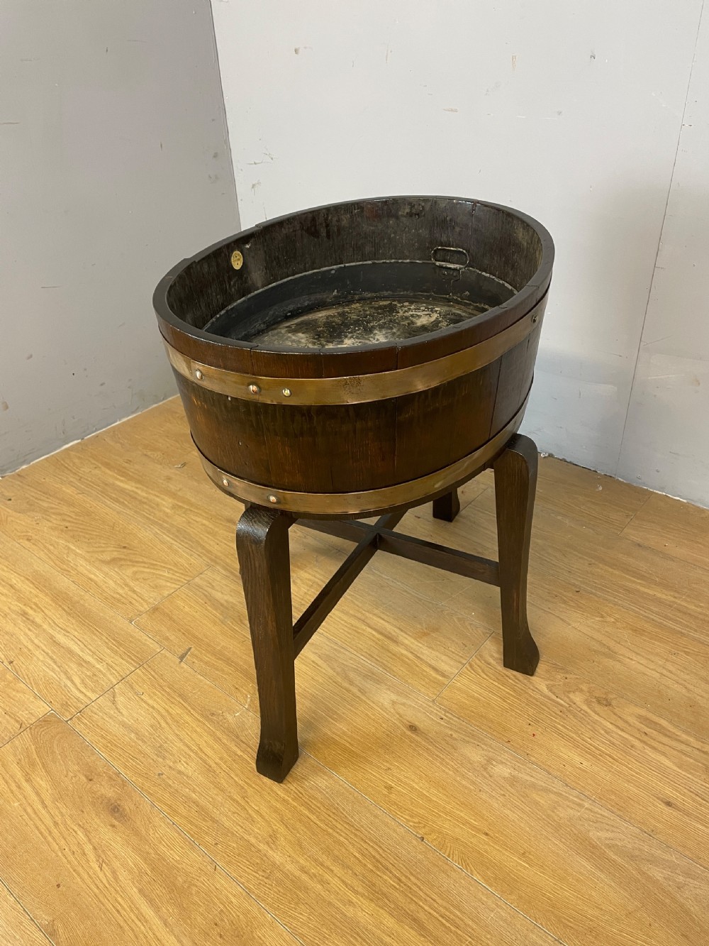 An Edwardian dark oak coopered circular planter with polished brass binding bands, raised on a three-legged wooden stand. View VIII