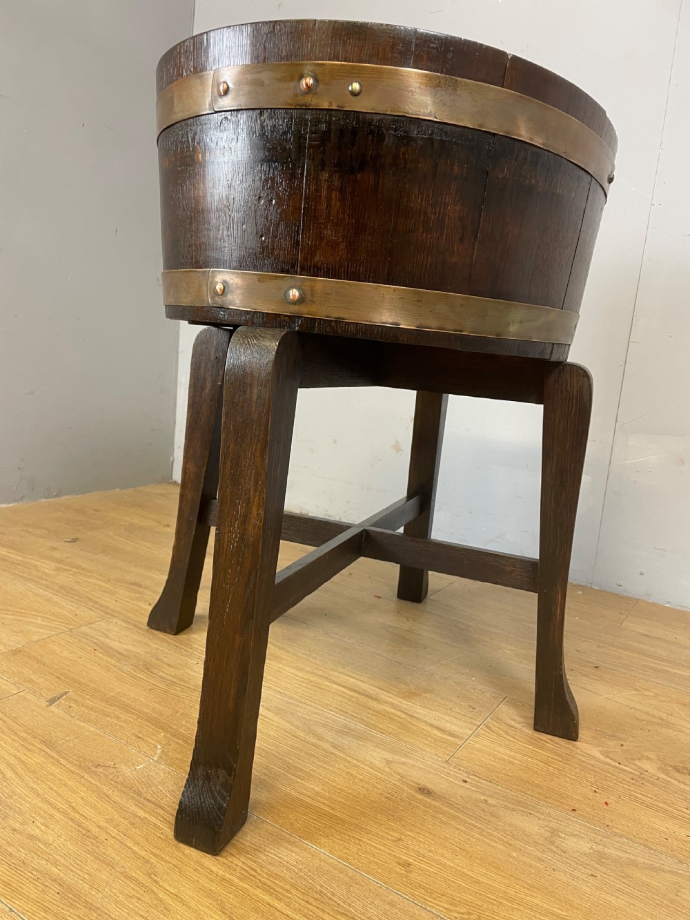 An Edwardian dark oak coopered circular planter with polished brass binding bands, raised on a three-legged wooden stand. View IX