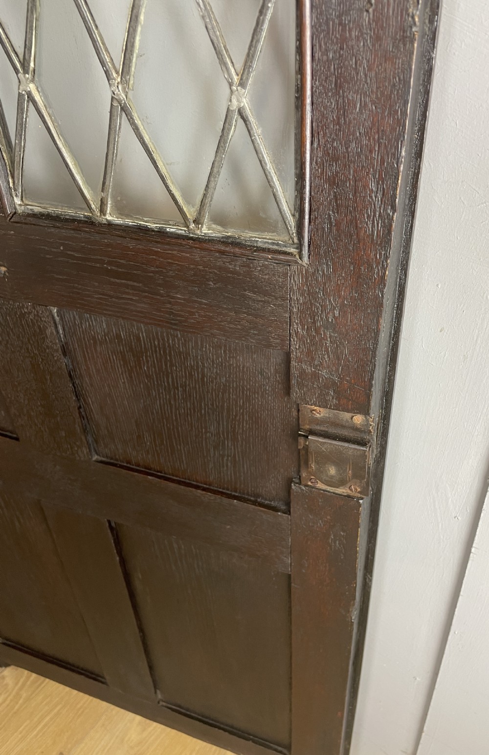 An early eighteenth-century dark oak corner cupboard featuring an arched top, leaded diamond glass door, and raised lower panels. View III