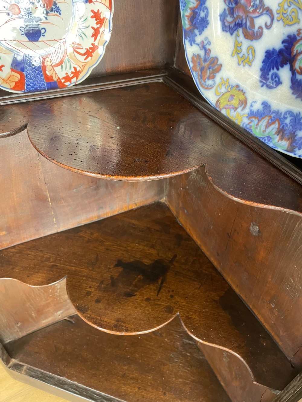 An early eighteenth-century dark oak corner cupboard featuring an arched top, leaded diamond glass door, and raised lower panels. View V
