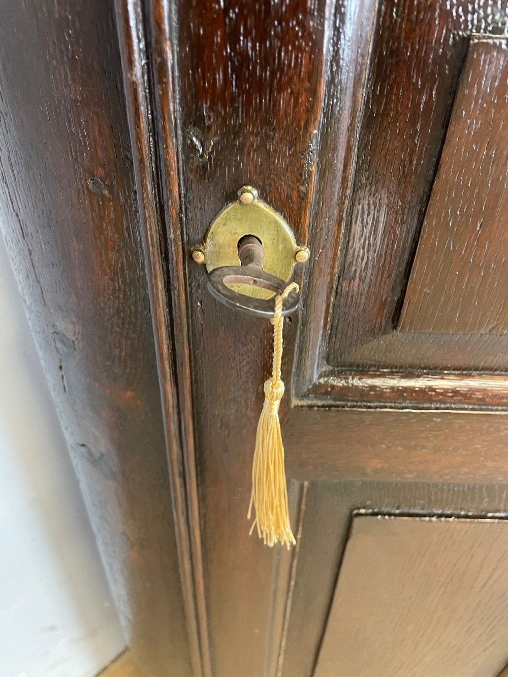 An early eighteenth-century dark oak corner cupboard featuring an arched top, leaded diamond glass door, and raised lower panels. View VIII
