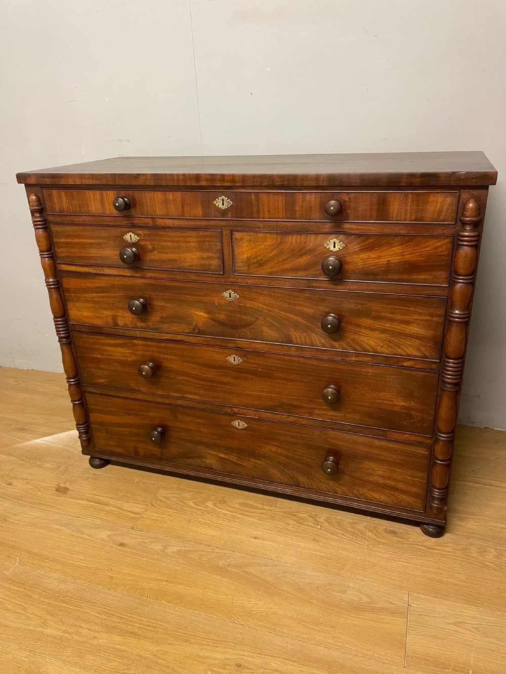 A Late Regency flame mahogany five-height chest of drawers with turned side columns, turned wooden knobs, and brass escutcheons.