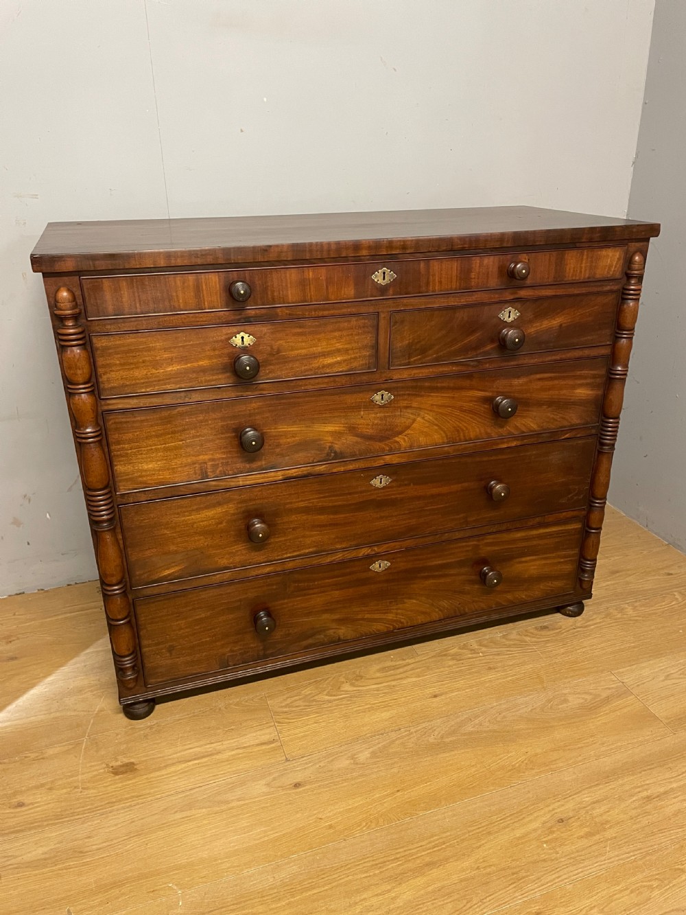 A Late Regency flame mahogany five-height chest of drawers with turned side columns, turned wooden knobs, and brass escutcheons. View II