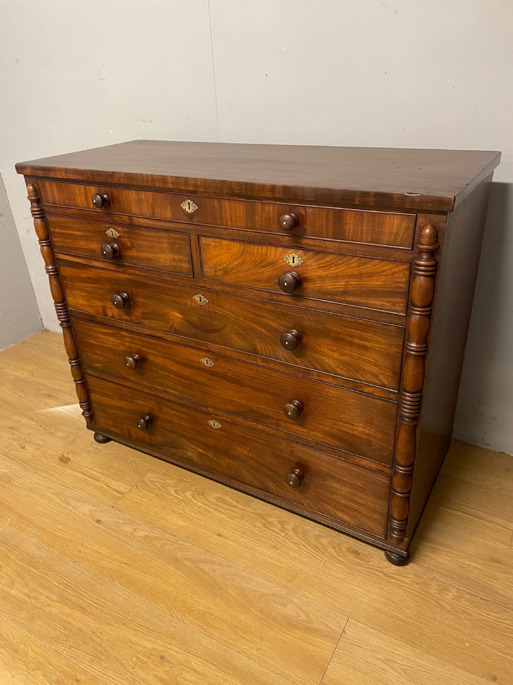 A Late Regency flame mahogany five-height chest of drawers with turned side columns, turned wooden knobs, and brass escutcheons. View III