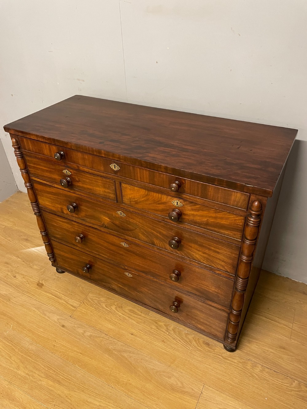 A Late Regency flame mahogany five-height chest of drawers with turned side columns, turned wooden knobs, and brass escutcheons. View V