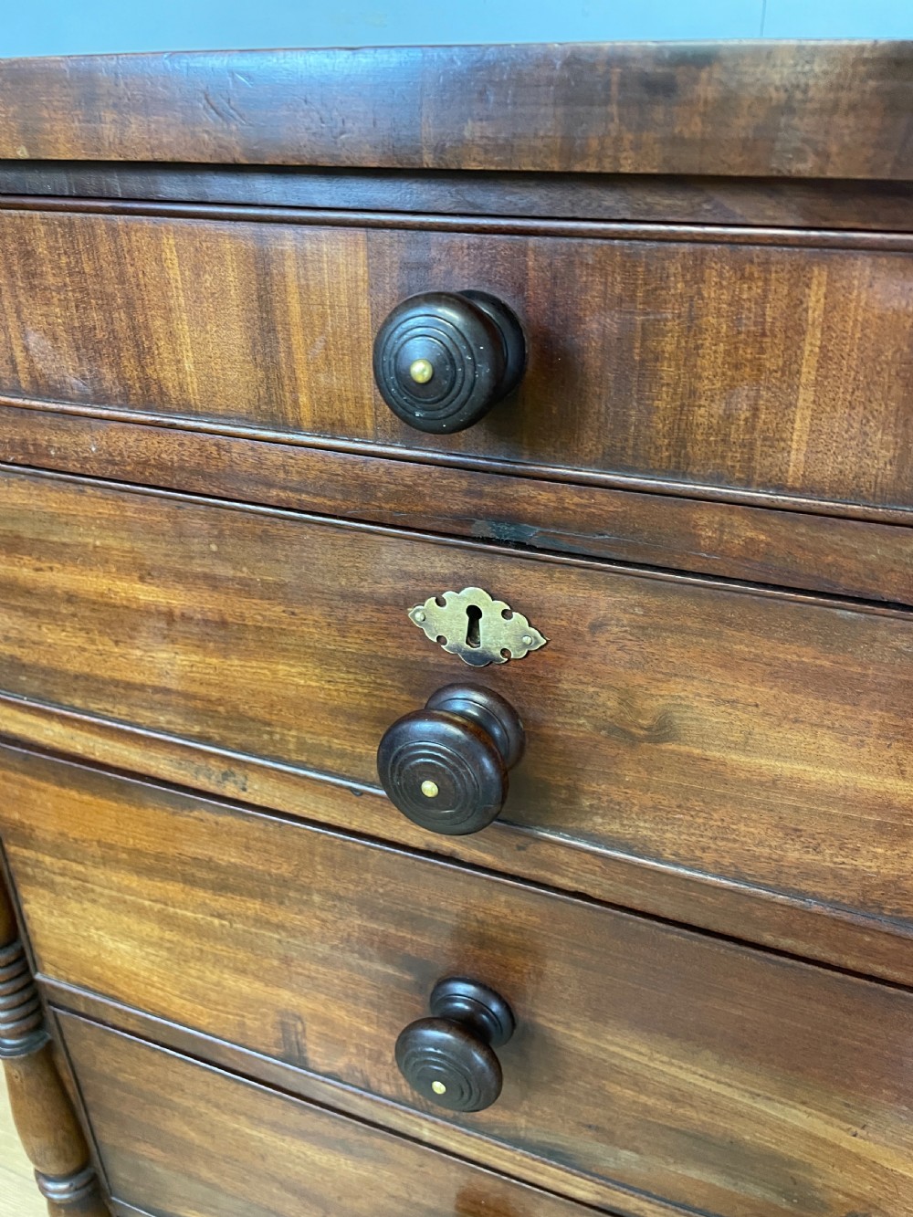 A Late Regency flame mahogany five-height chest of drawers with turned side columns, turned wooden knobs, and brass escutcheons. View VII