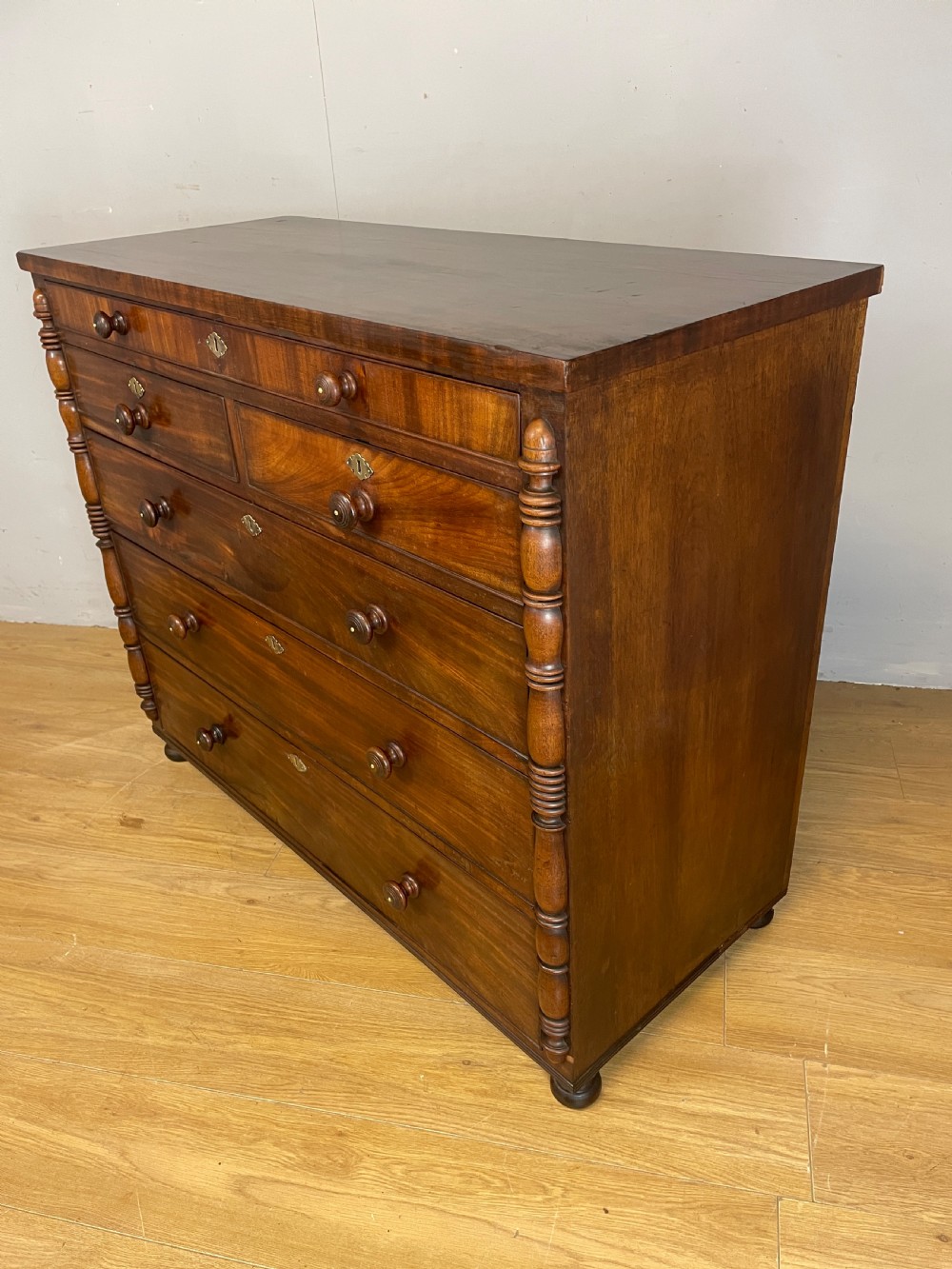 A Late Regency flame mahogany five-height chest of drawers with turned side columns, turned wooden knobs, and brass escutcheons. View VIII