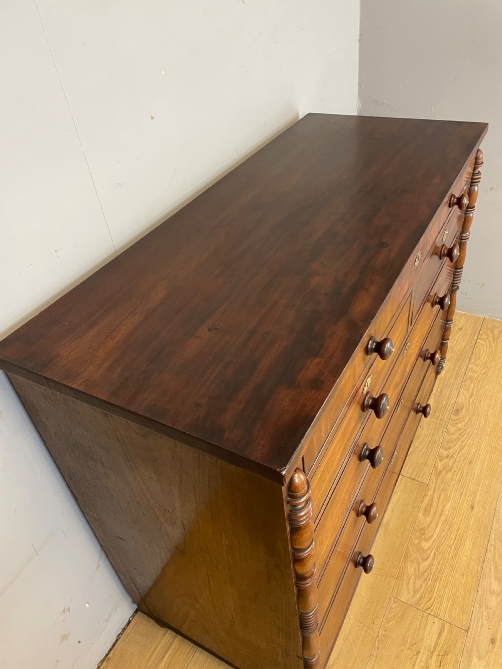A Late Regency flame mahogany five-height chest of drawers with turned side columns, turned wooden knobs, and brass escutcheons. View X