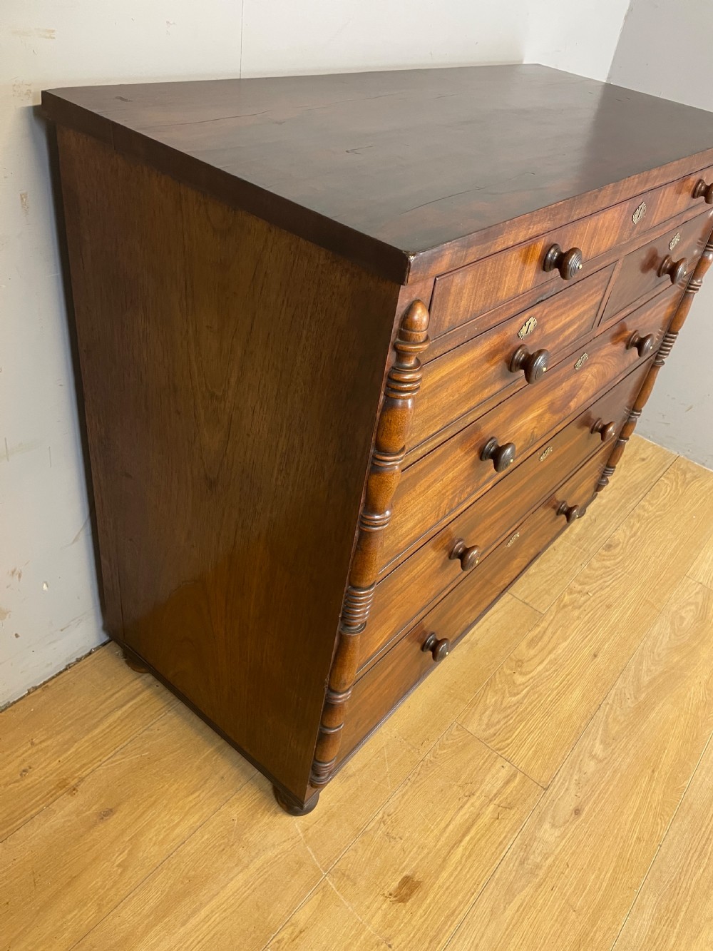 A Late Regency flame mahogany five-height chest of drawers with turned side columns, turned wooden knobs, and brass escutcheons. View XI