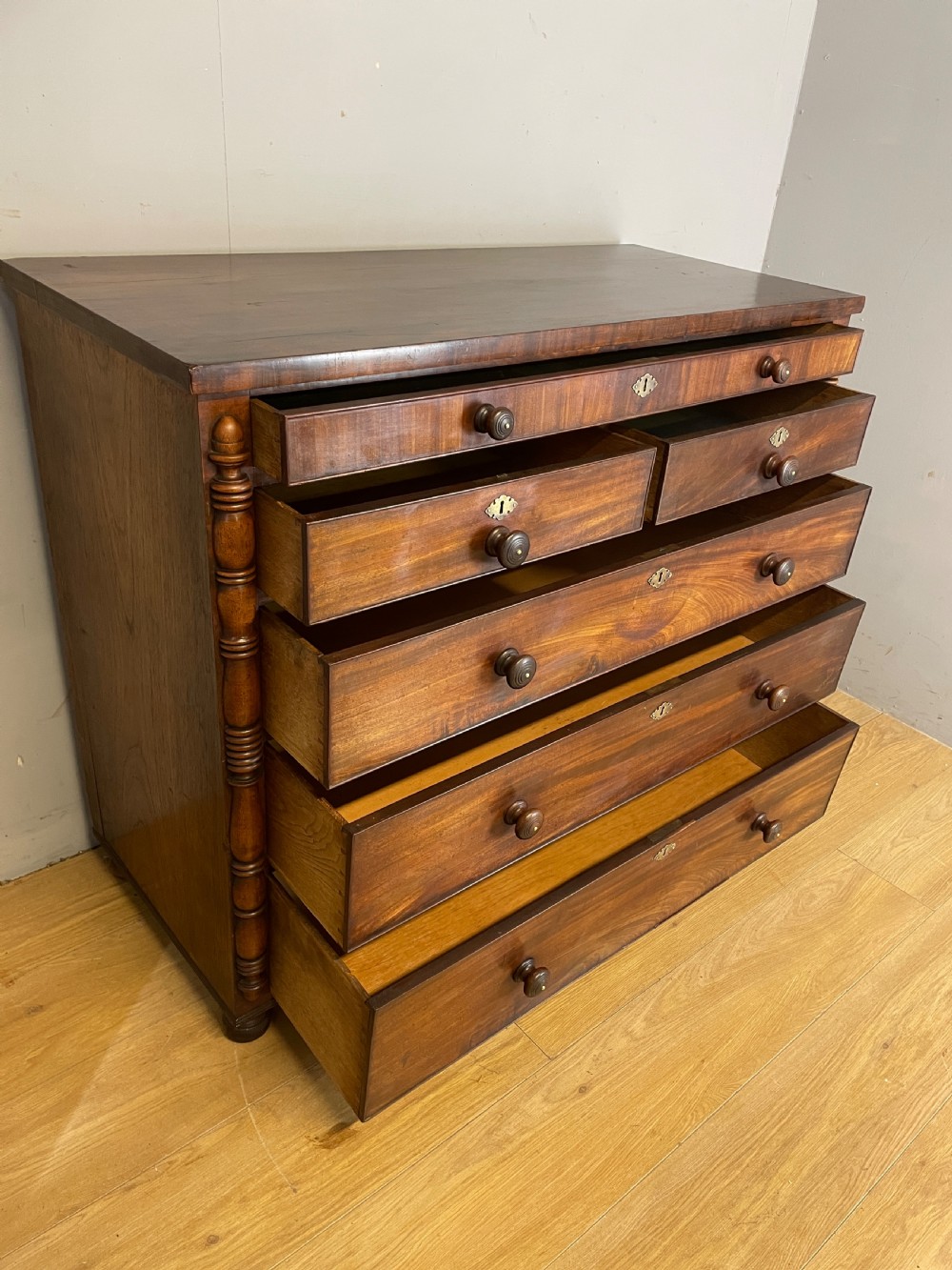 A Late Regency flame mahogany five-height chest of drawers with turned side columns, turned wooden knobs, and brass escutcheons. View XII