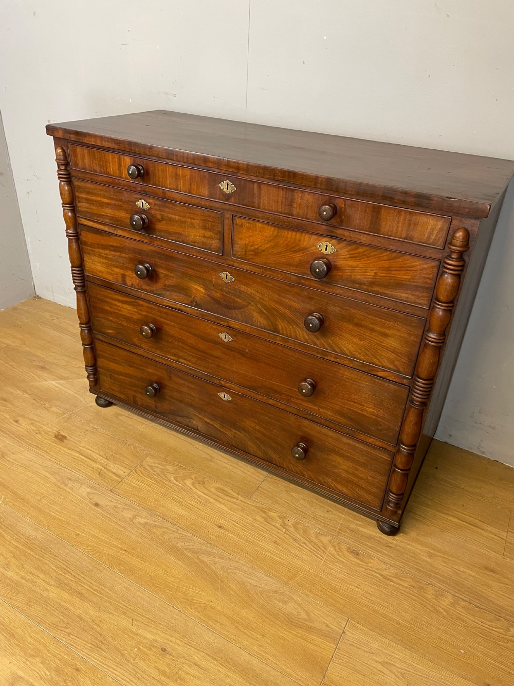 A Late Regency flame mahogany five-height chest of drawers with turned side columns, turned wooden knobs, and brass escutcheons. View XIII