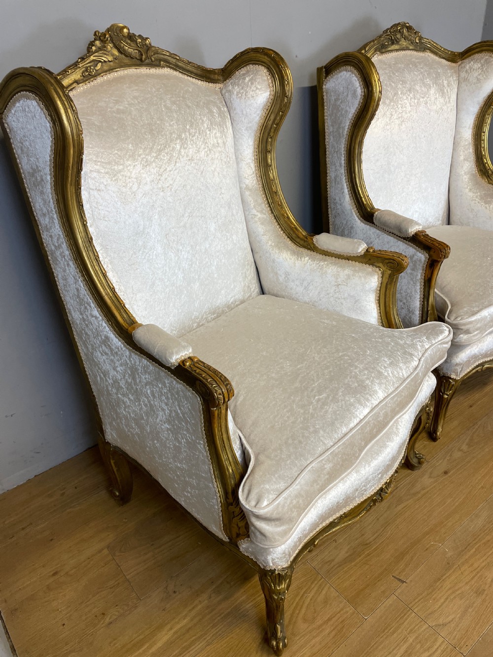 A pair of early twentieth-century French winged armchairs with carved gilded wooden frames and cream velvet upholstery. View IV
