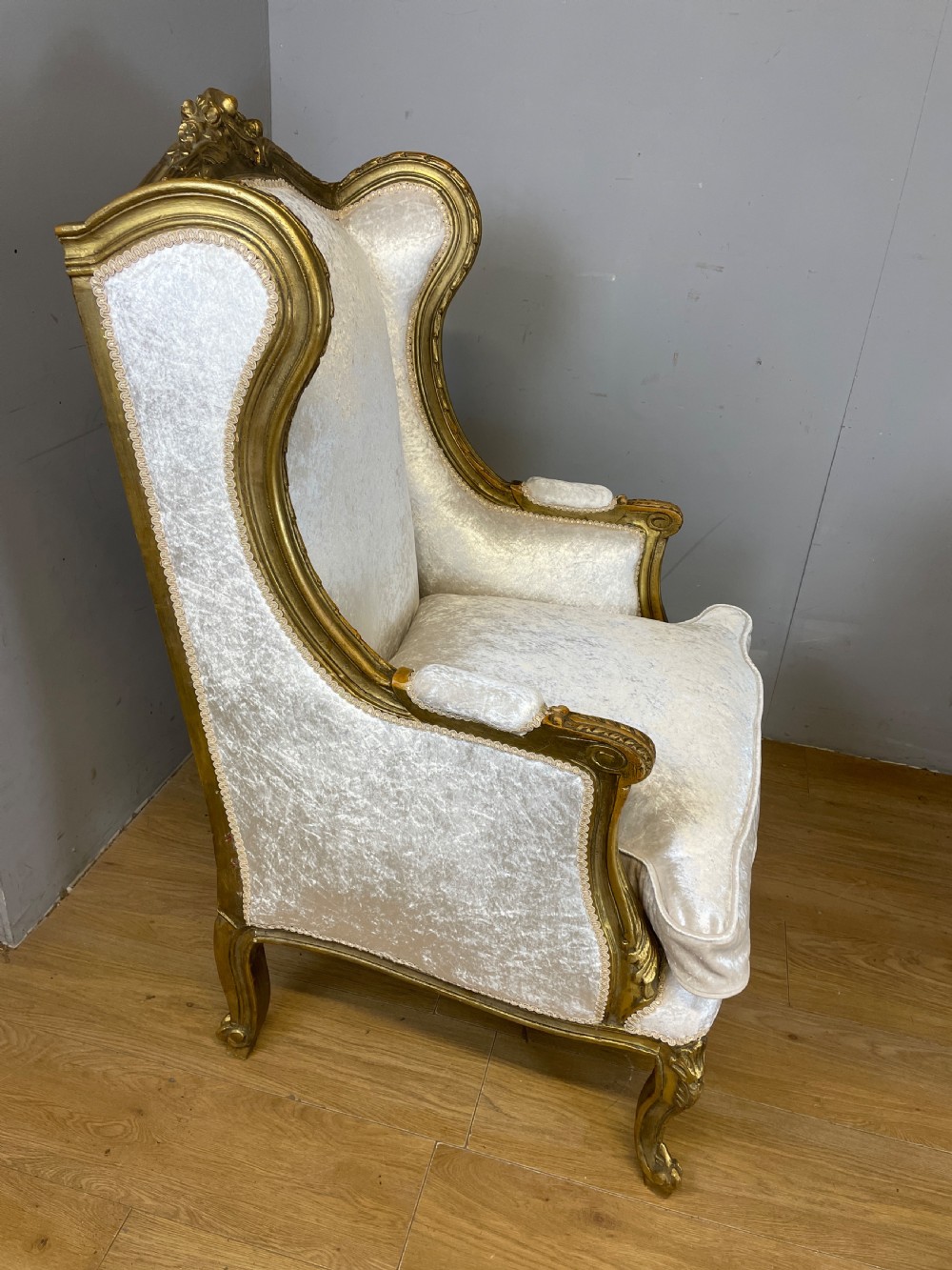 A pair of early twentieth-century French winged armchairs with carved gilded wooden frames and cream velvet upholstery. View VI