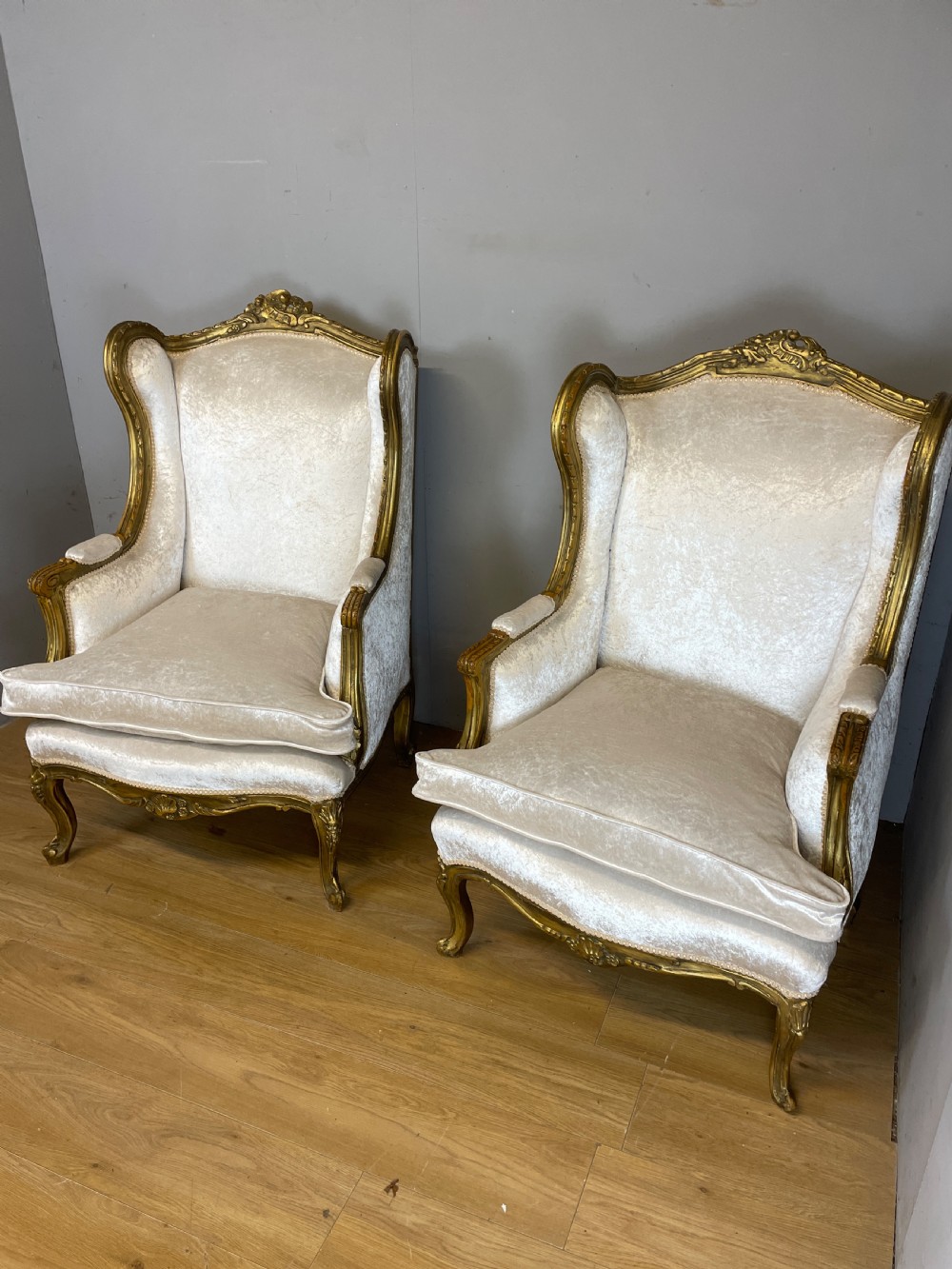 A pair of early twentieth-century French winged armchairs with carved gilded wooden frames and cream velvet upholstery. View X