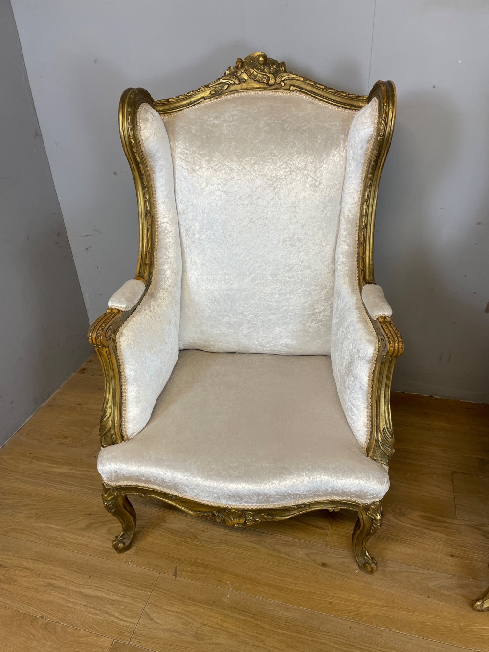 A pair of early twentieth-century French winged armchairs with carved gilded wooden frames and cream velvet upholstery. View XII