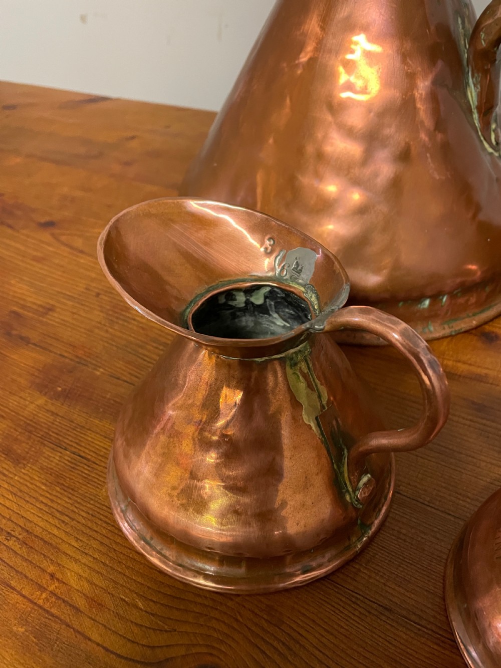 A set of seven graduated Georgian copper measuring jugs featuring haystack bodies and loop handles arranged by size on a wooden surface. View VII