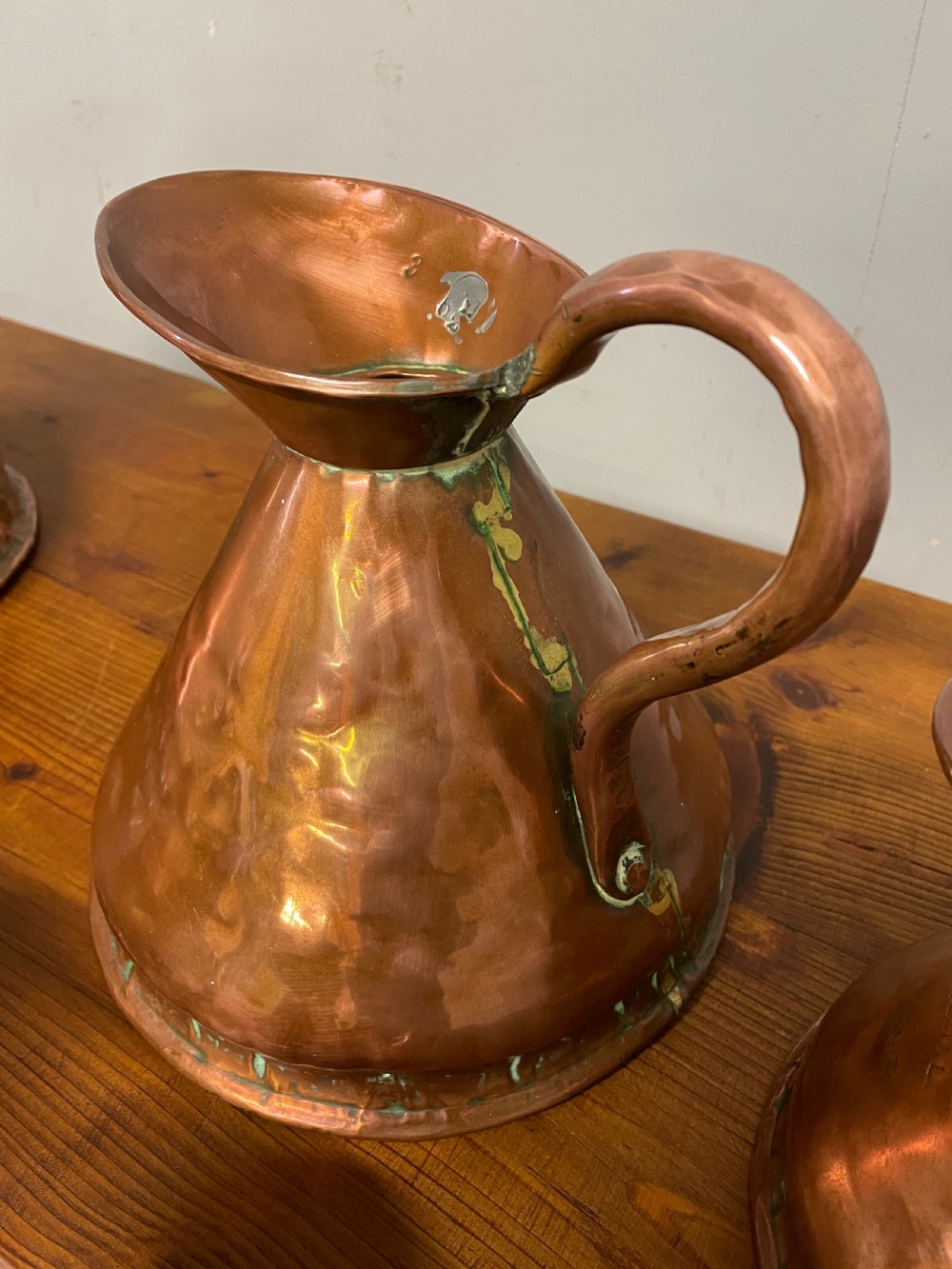 A set of seven graduated Georgian copper measuring jugs featuring haystack bodies and loop handles arranged by size on a wooden surface. View XIV