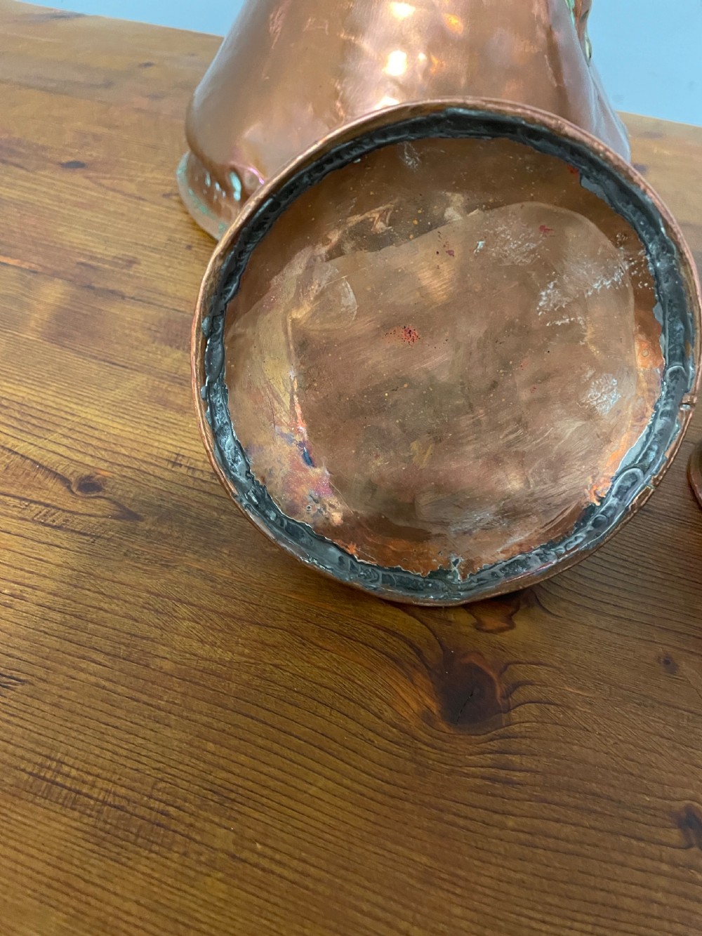 A set of seven graduated Georgian copper measuring jugs featuring haystack bodies and loop handles arranged by size on a wooden surface. View XV