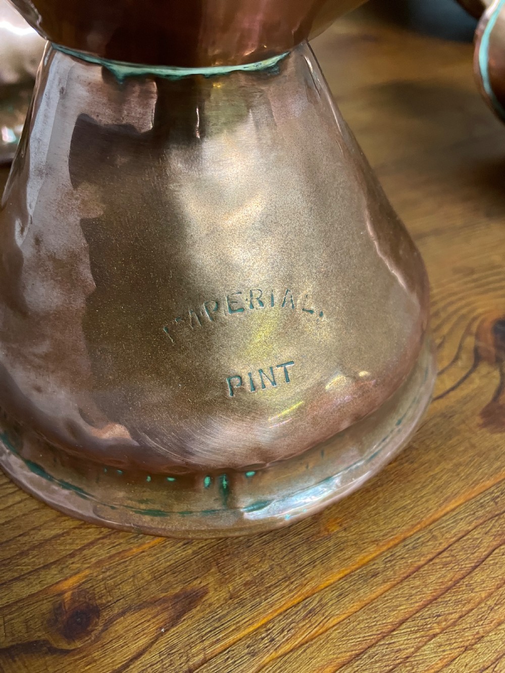 A set of seven graduated Georgian copper measuring jugs featuring haystack bodies and loop handles arranged by size on a wooden surface. View XX