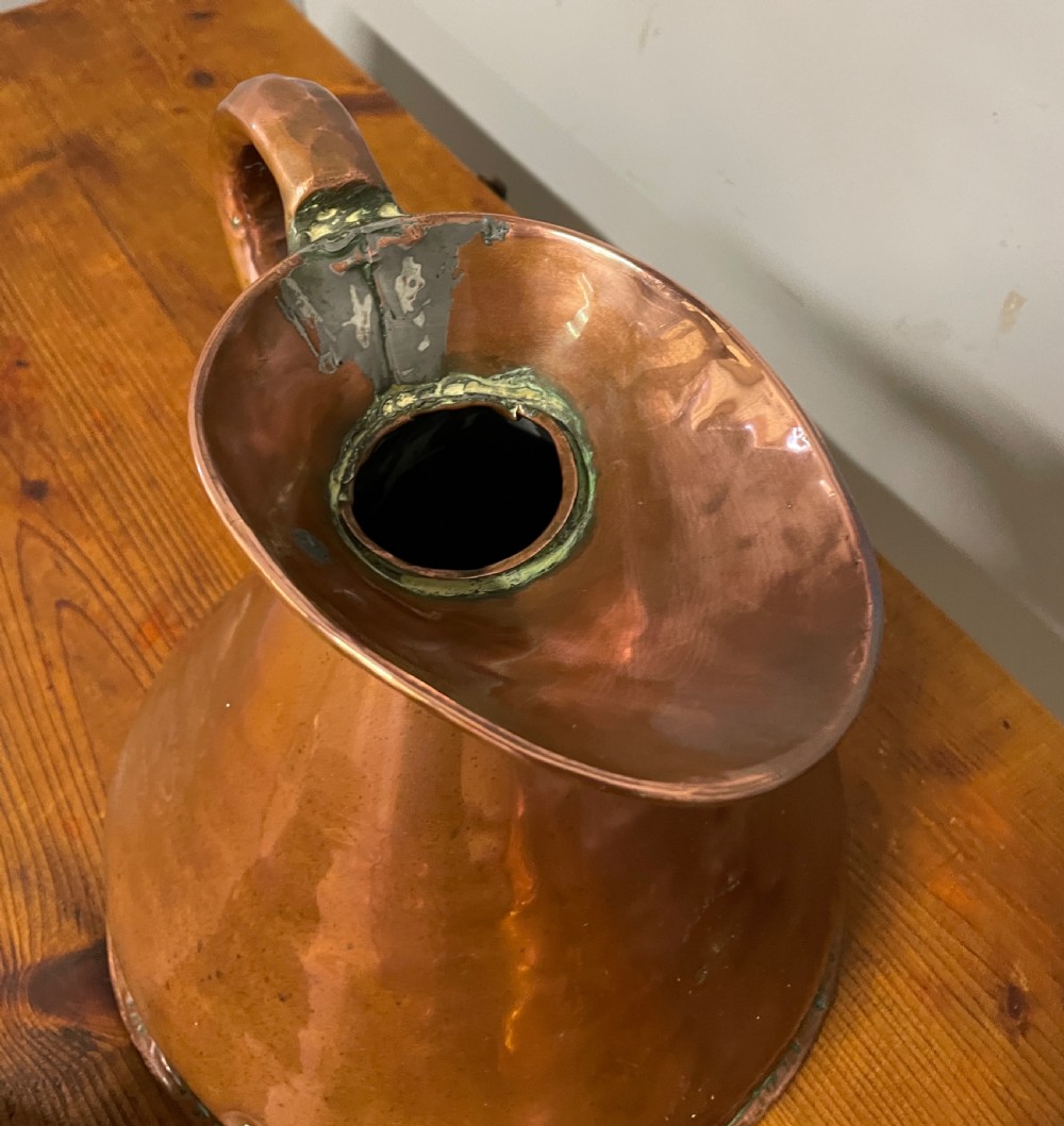A set of seven graduated Georgian copper measuring jugs featuring haystack bodies and loop handles arranged by size on a wooden surface. View XXII
