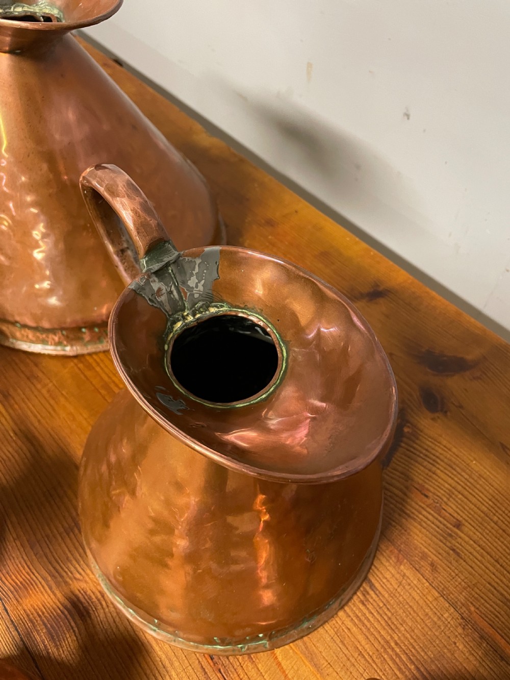 A set of seven graduated Georgian copper measuring jugs featuring haystack bodies and loop handles arranged by size on a wooden surface. View XXIII