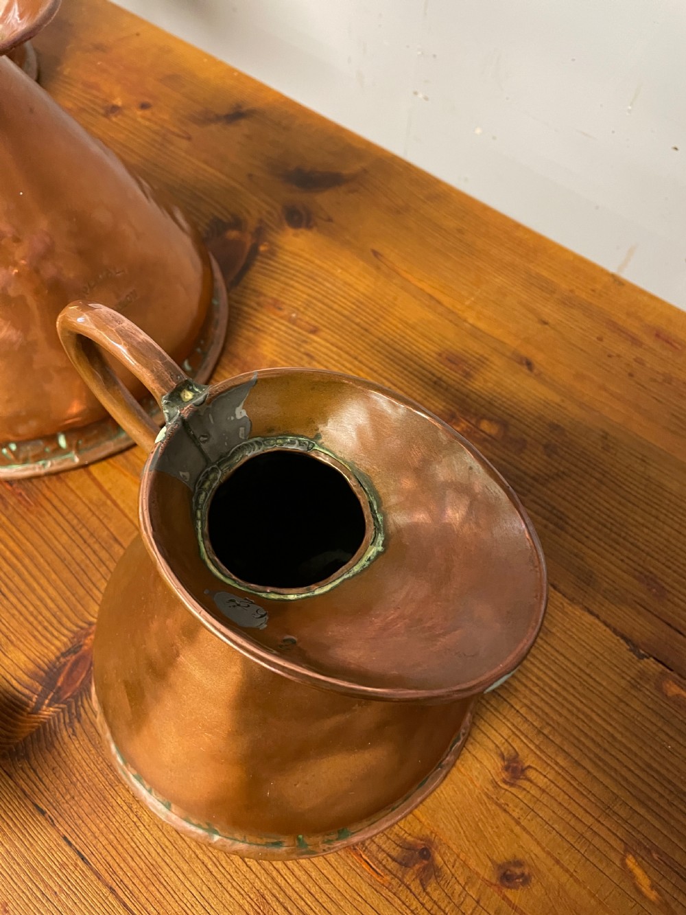 A set of seven graduated Georgian copper measuring jugs featuring haystack bodies and loop handles arranged by size on a wooden surface. View XXV
