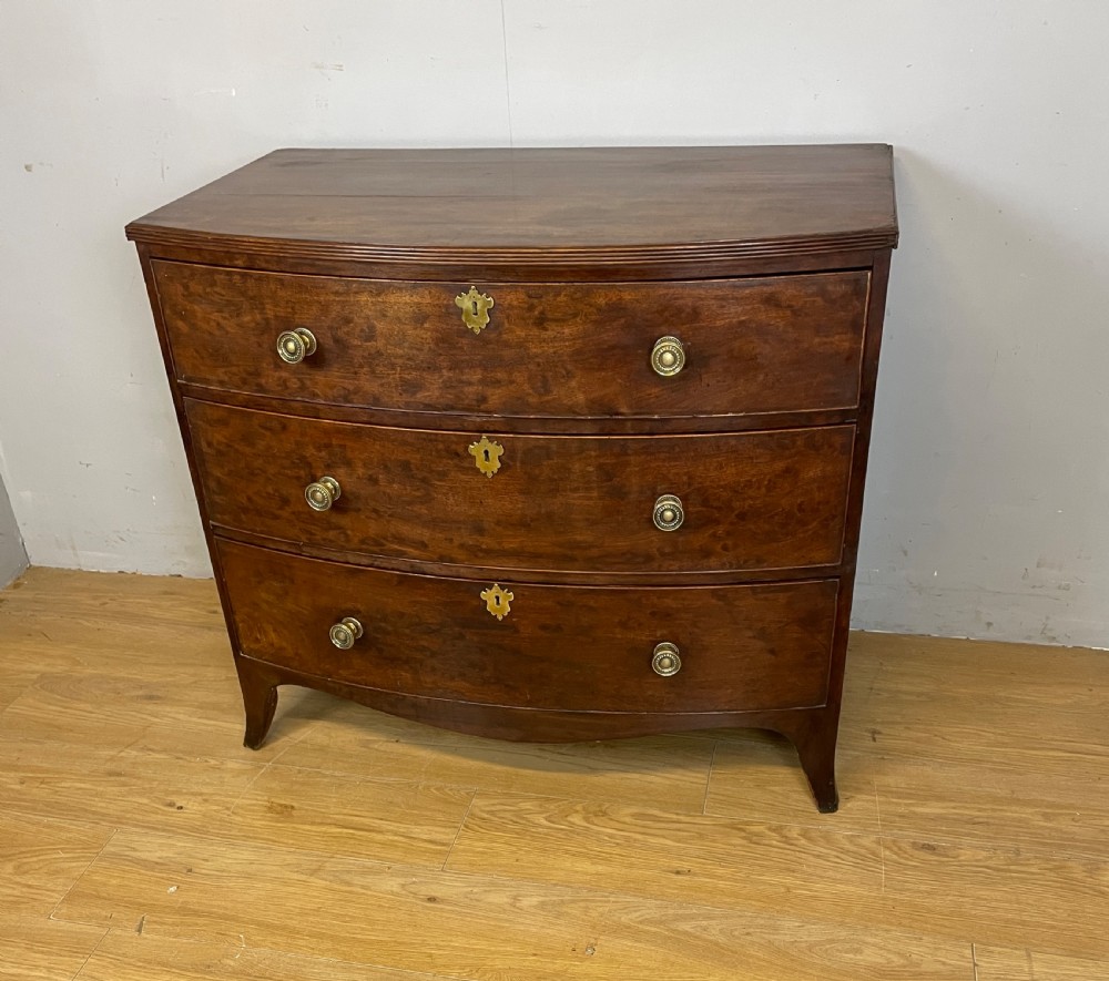 An antique Regency mahogany bow-front chest of drawers featuring three long drawers with brass knobs, brass keyhole escutcheons, and curved bracket feet. View II