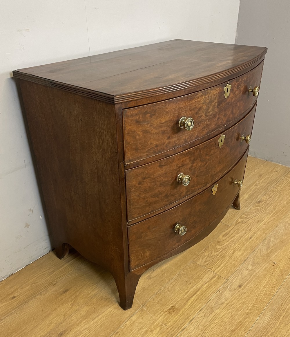 An antique Regency mahogany bow-front chest of drawers featuring three long drawers with brass knobs, brass keyhole escutcheons, and curved bracket feet. View III