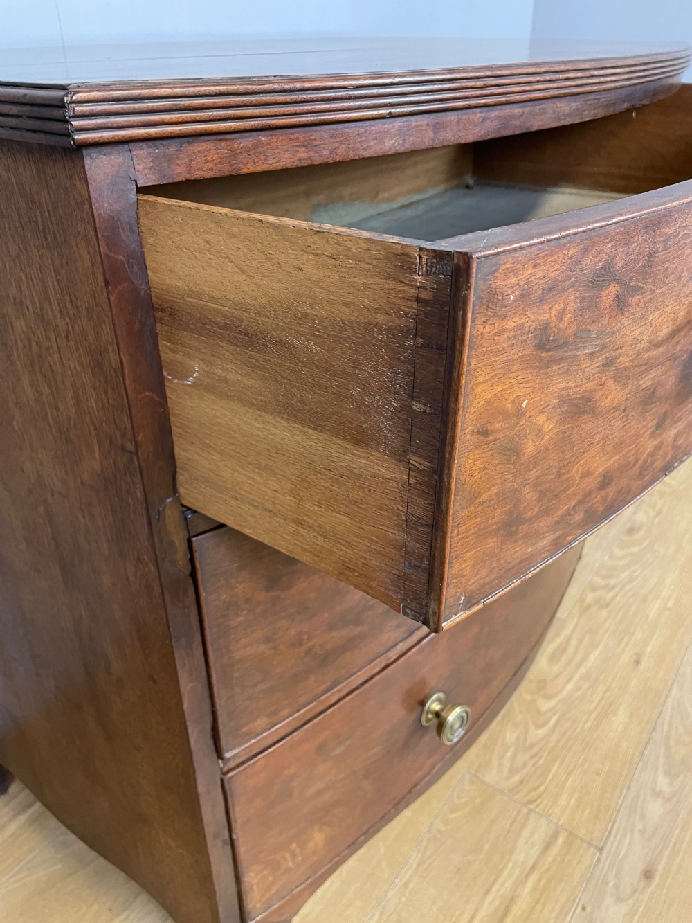 An antique Regency mahogany bow-front chest of drawers featuring three long drawers with brass knobs, brass keyhole escutcheons, and curved bracket feet. View V