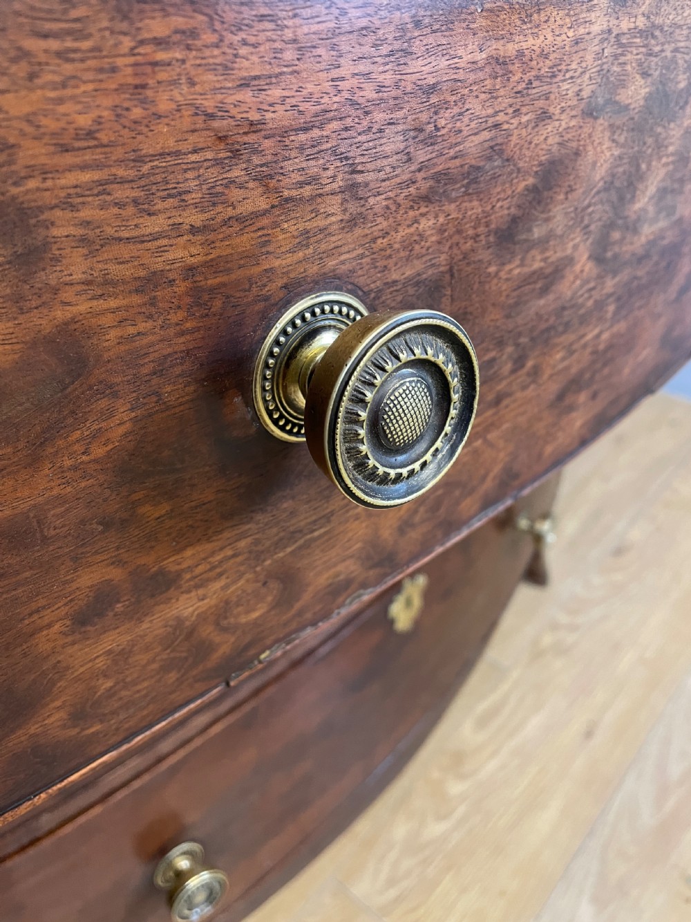 An antique Regency mahogany bow-front chest of drawers featuring three long drawers with brass knobs, brass keyhole escutcheons, and curved bracket feet. View VII