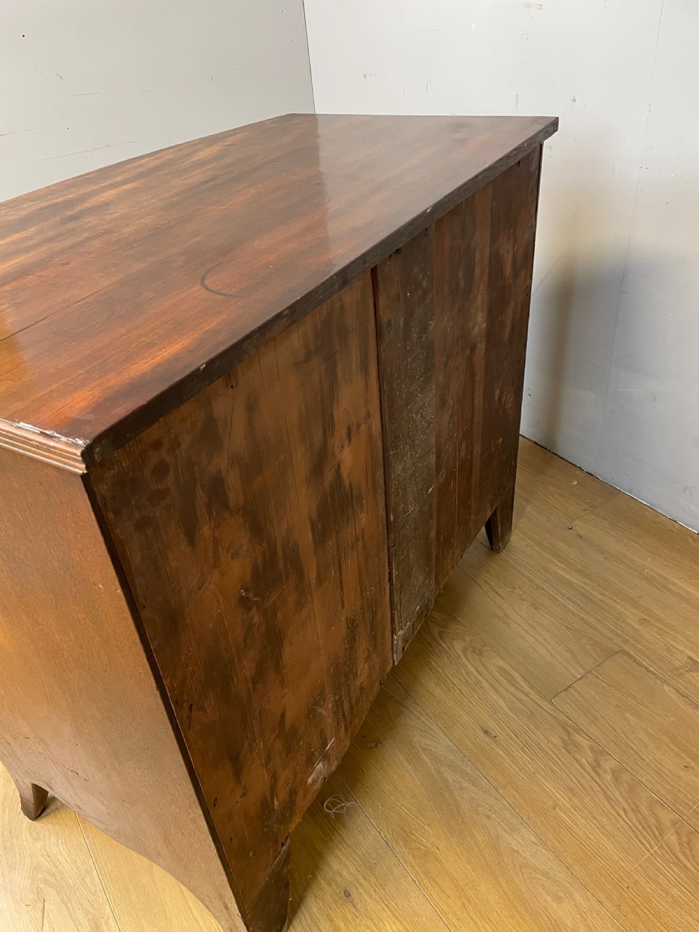 An antique Regency mahogany bow-front chest of drawers featuring three long drawers with brass knobs, brass keyhole escutcheons, and curved bracket feet. View XII