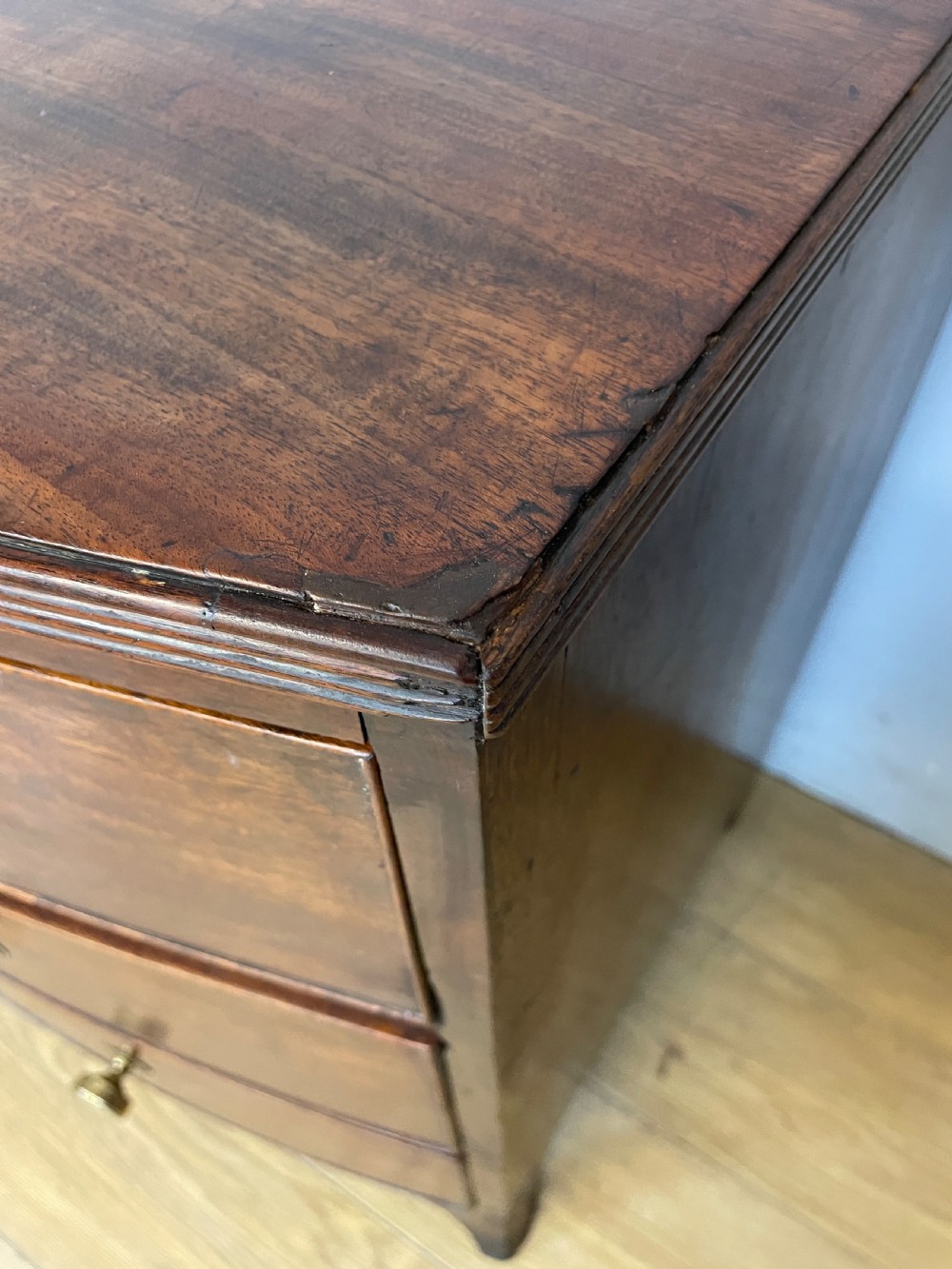 An antique Regency mahogany bow-front chest of drawers featuring three long drawers with brass knobs, brass keyhole escutcheons, and curved bracket feet. View XIII
