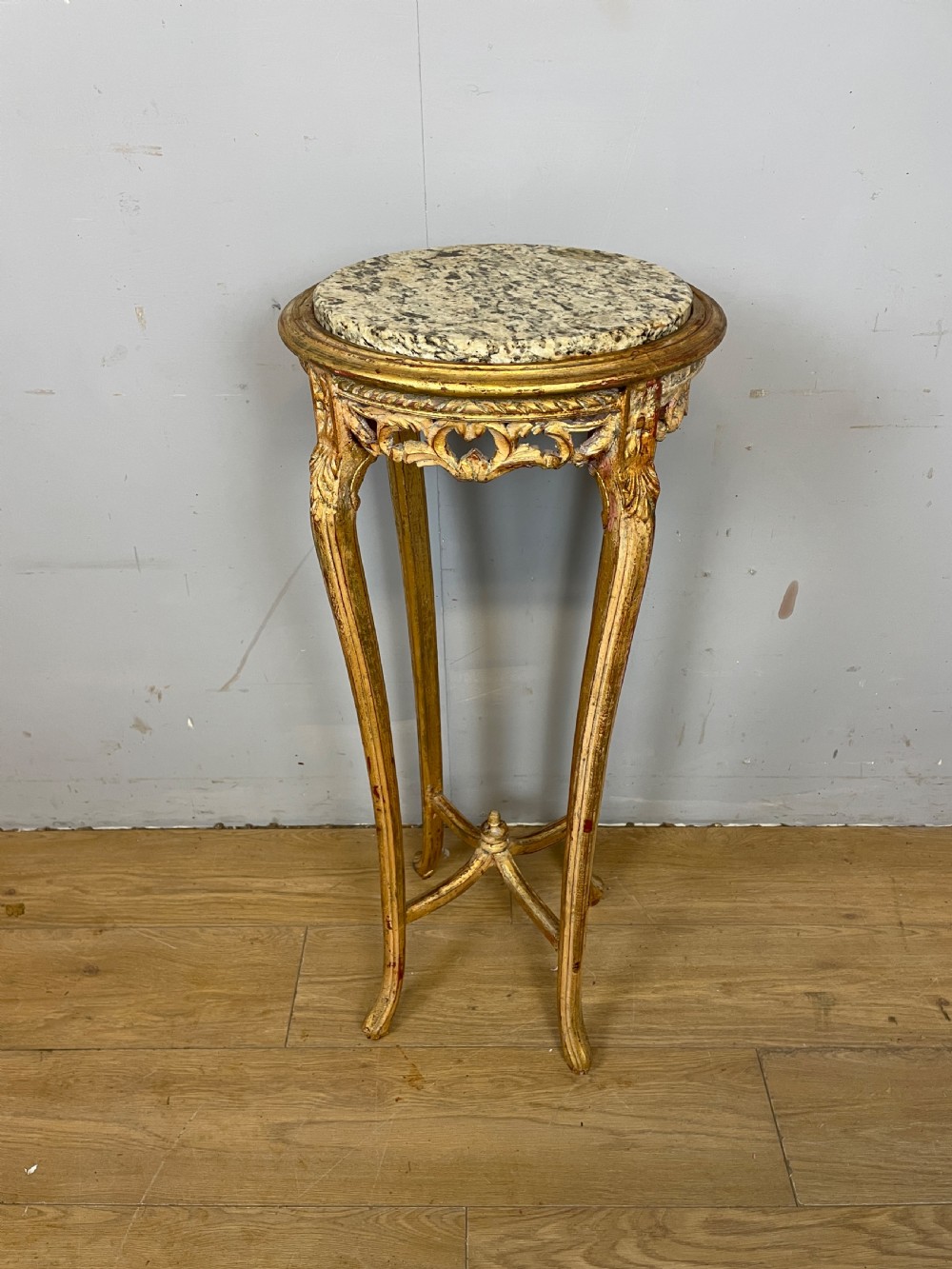 An Edwardian carved giltwood torchere featuring a circular grey marble top, slender cabriole legs, pierced aprons, and an X-frame stretcher.
