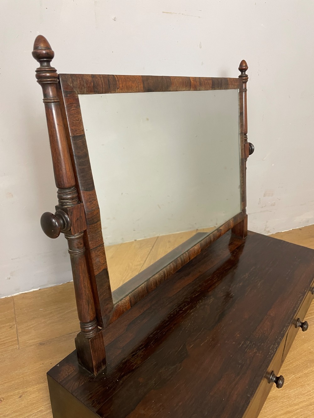 An early Victorian dark rosewood dressing table mirror featuring turned support columns, finials, and a rectangular swivelling frame resting on a plinth drawer base. View III