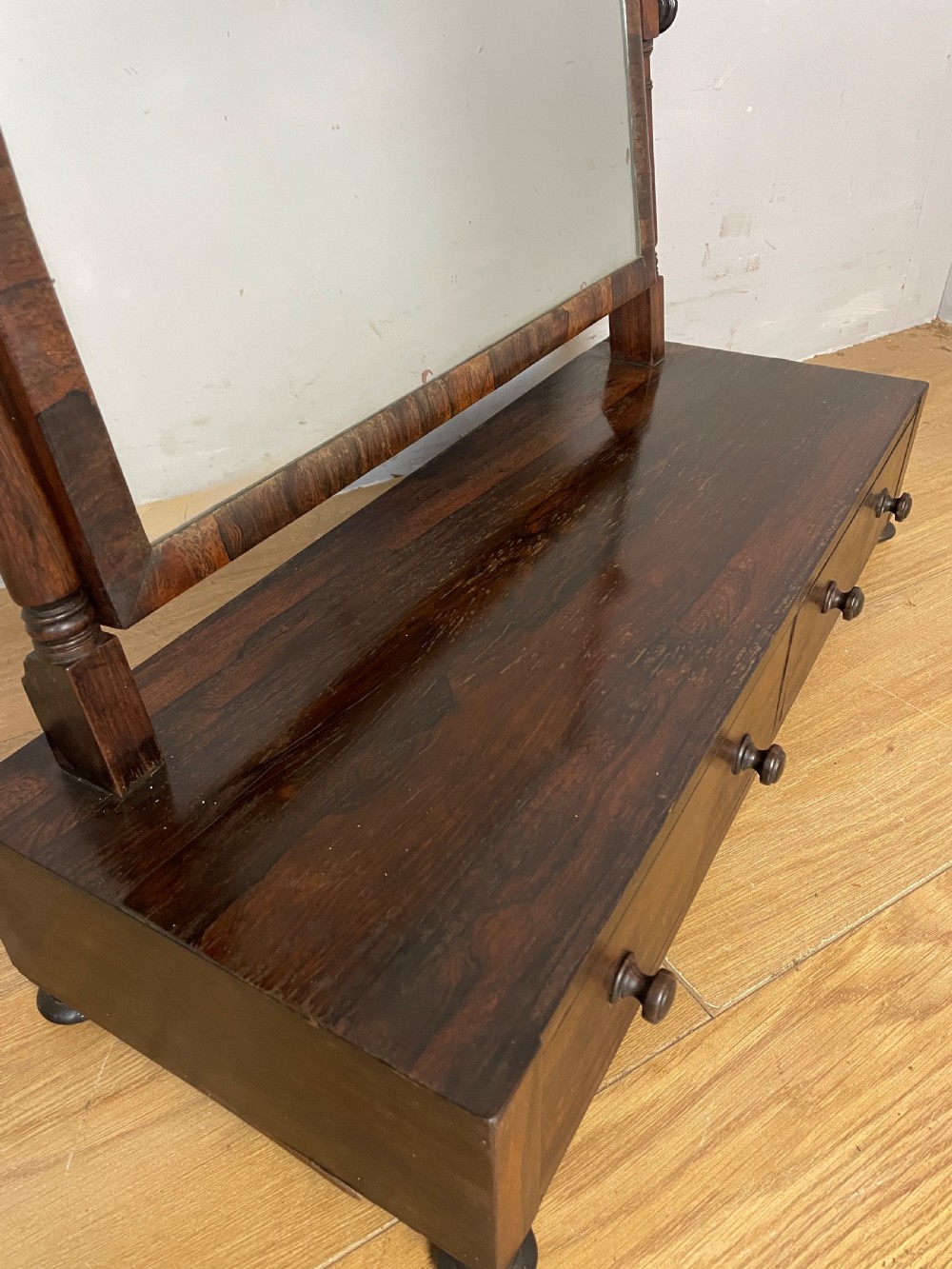 An early Victorian dark rosewood dressing table mirror featuring turned support columns, finials, and a rectangular swivelling frame resting on a plinth drawer base. View IV