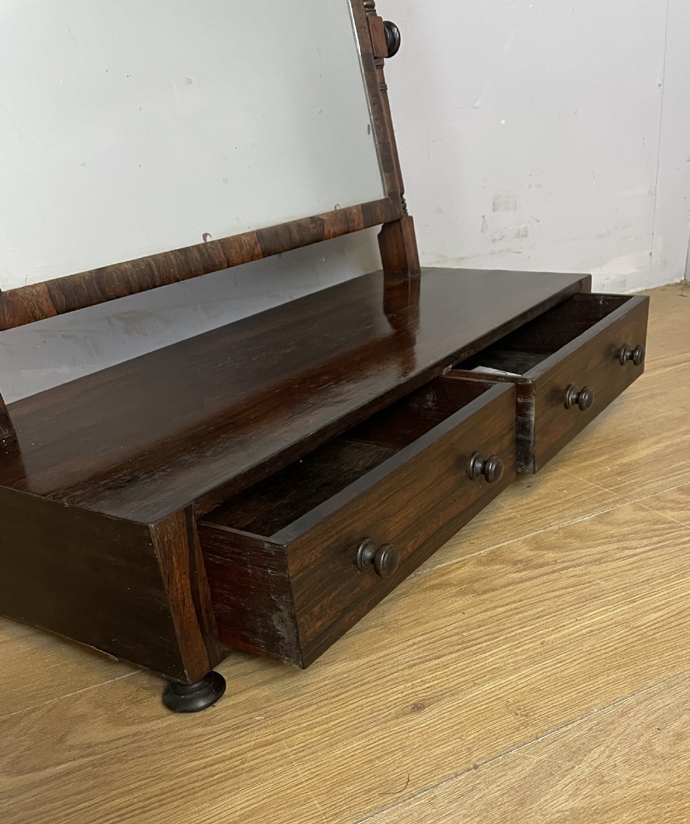 An early Victorian dark rosewood dressing table mirror featuring turned support columns, finials, and a rectangular swivelling frame resting on a plinth drawer base. View VI