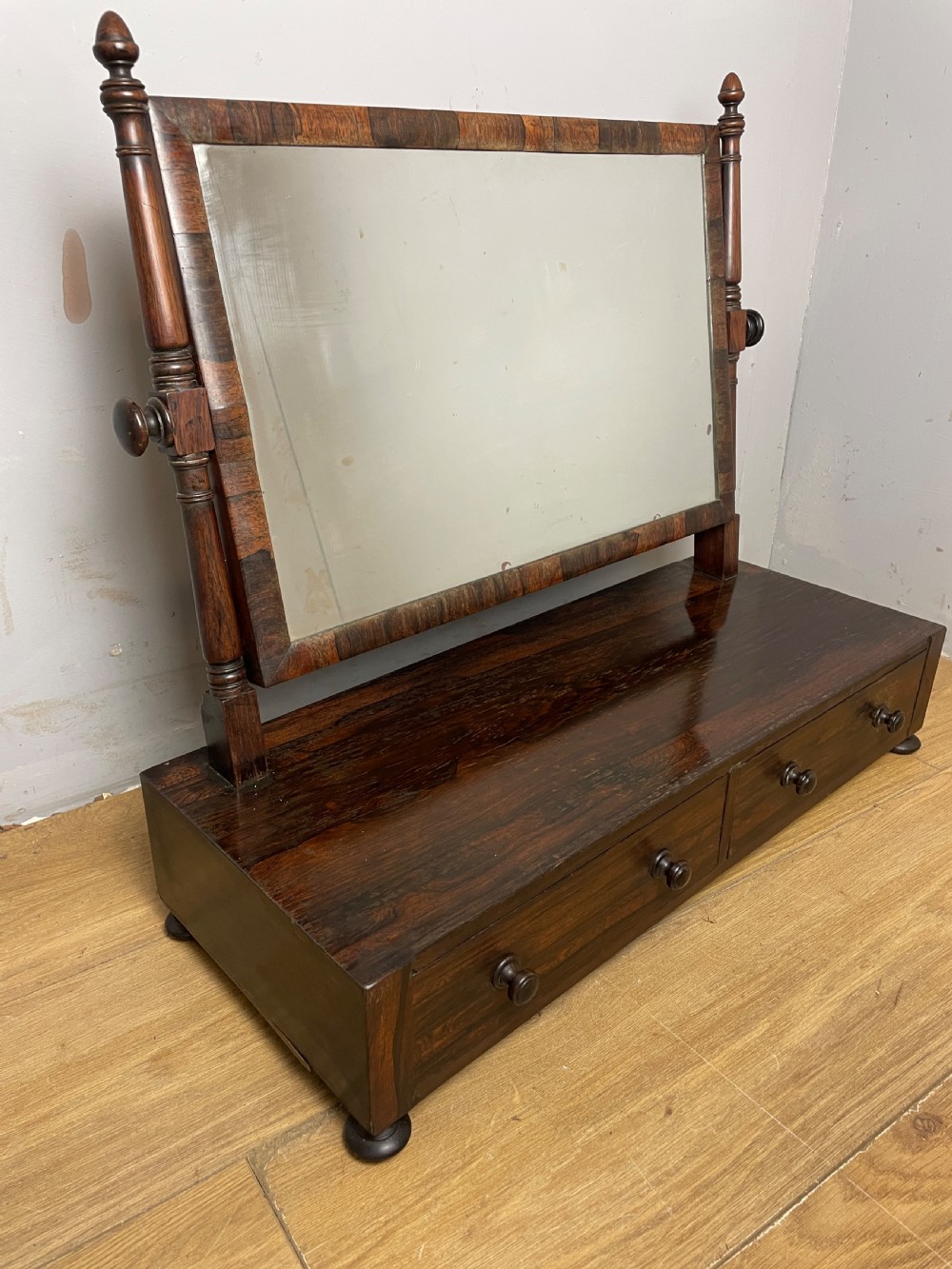 An early Victorian dark rosewood dressing table mirror featuring turned support columns, finials, and a rectangular swivelling frame resting on a plinth drawer base. View XI