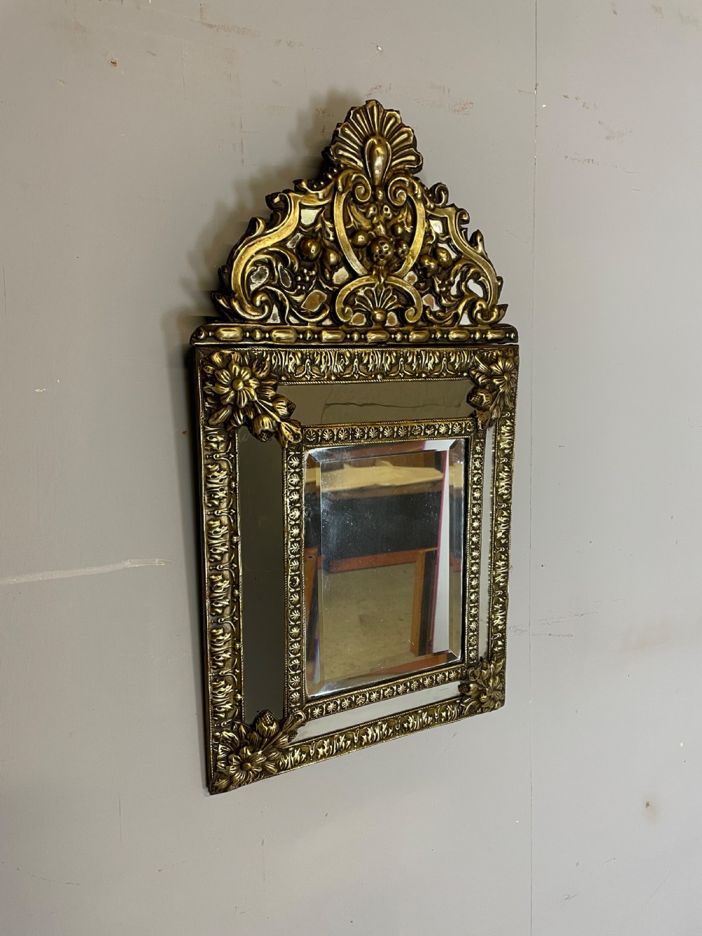 A nineteenth-century French cushion mirror featuring an ornate repousse brass frame with foliate cresting and bevelled mirror plates.
