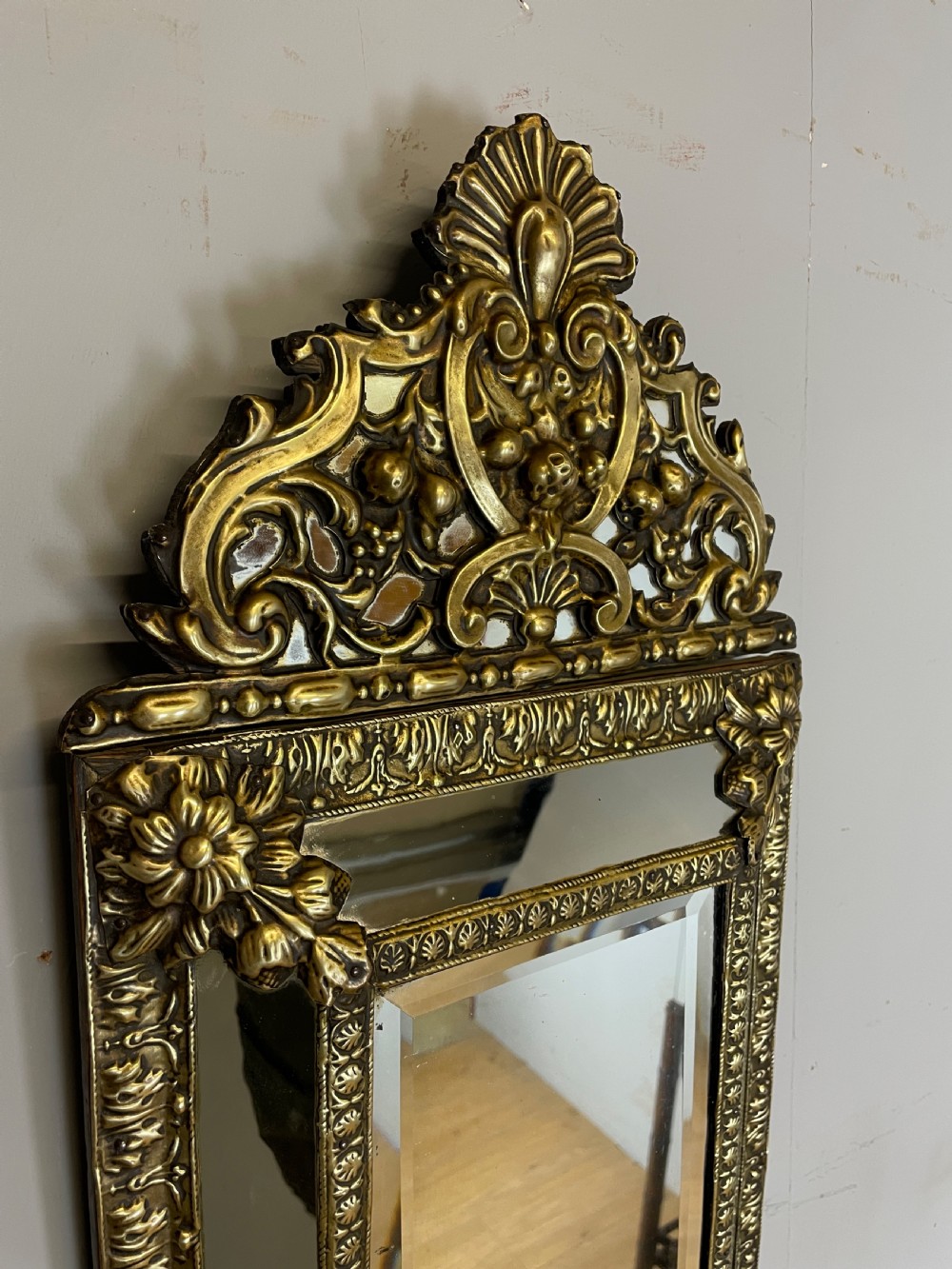 A nineteenth-century French cushion mirror featuring an ornate repousse brass frame with foliate cresting and bevelled mirror plates. View II