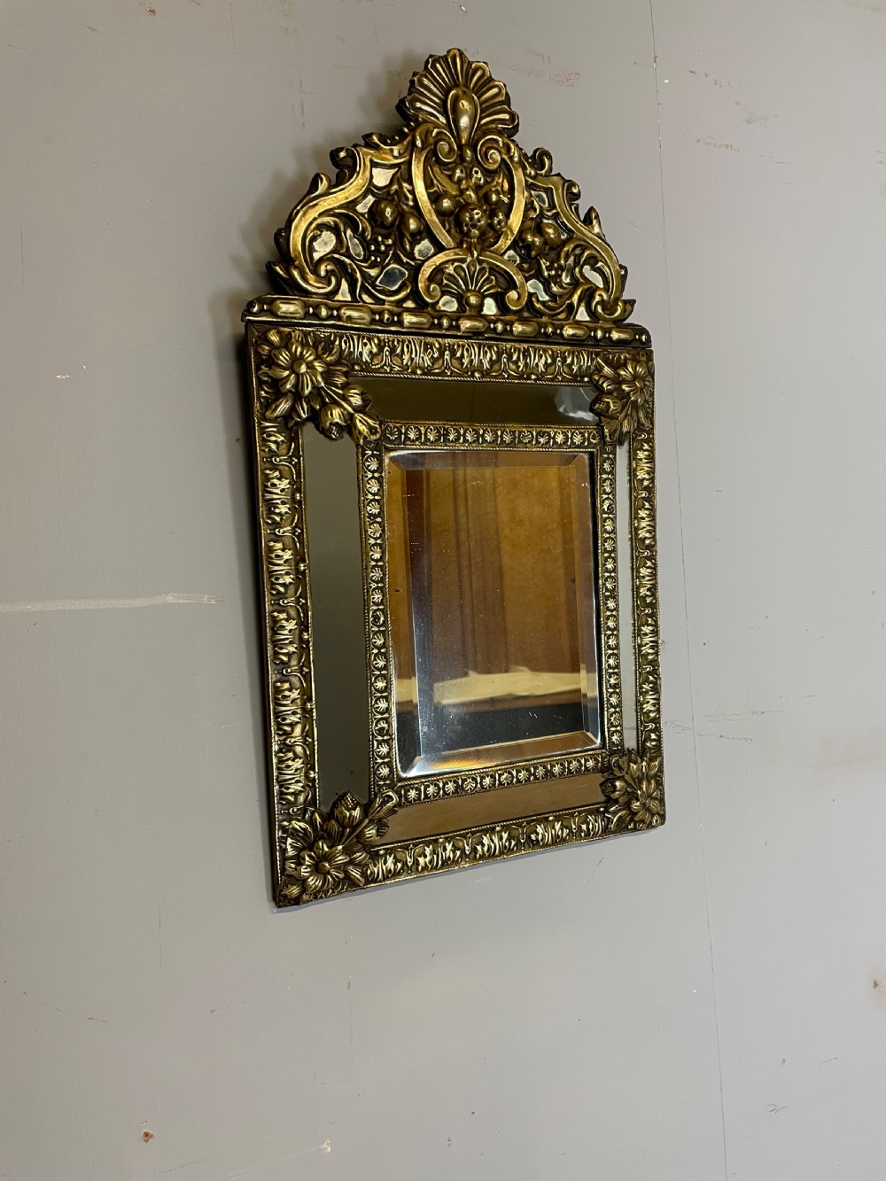 A nineteenth-century French cushion mirror featuring an ornate repousse brass frame with foliate cresting and bevelled mirror plates. View III