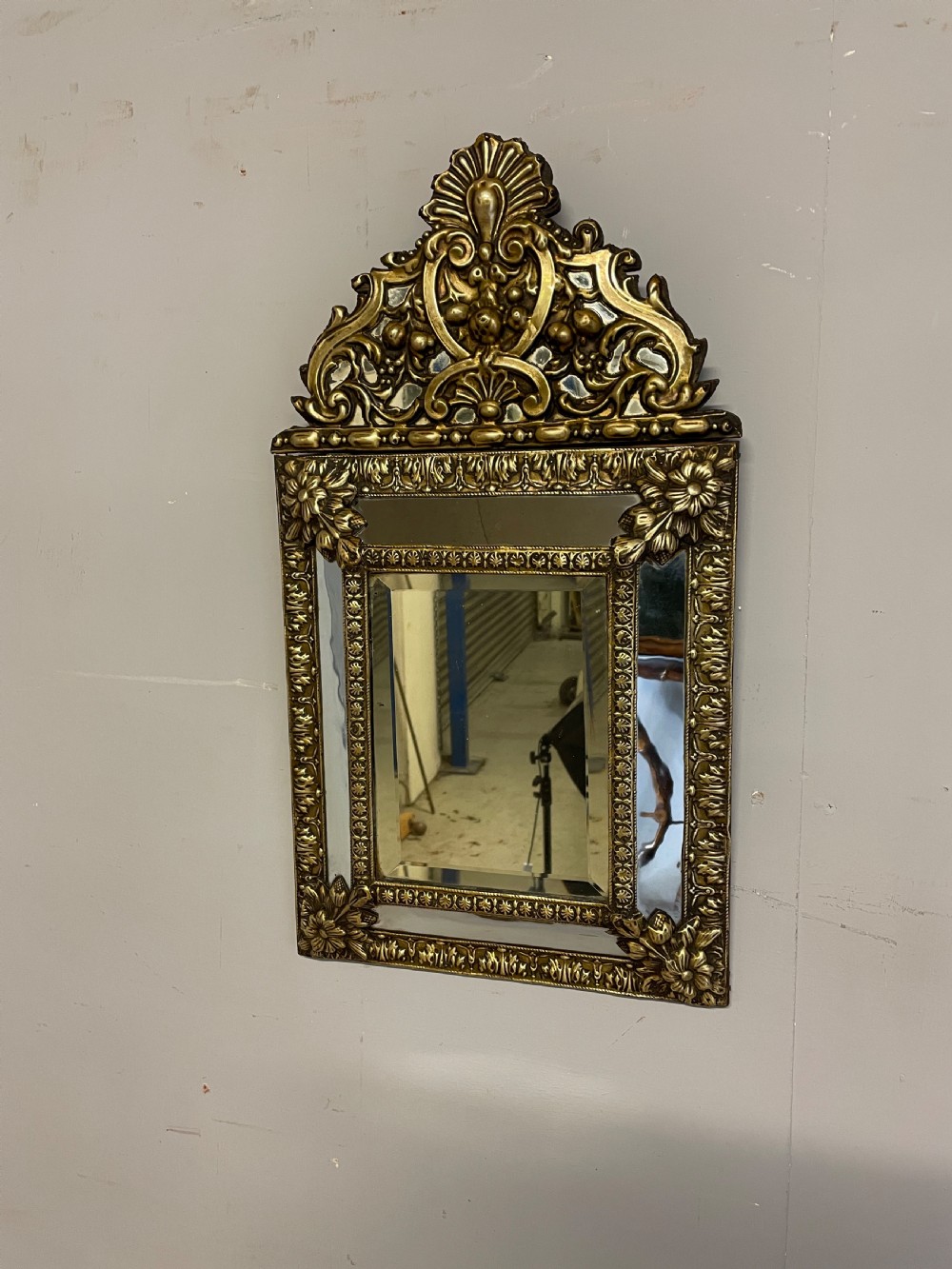 A nineteenth-century French cushion mirror featuring an ornate repousse brass frame with foliate cresting and bevelled mirror plates. View IV