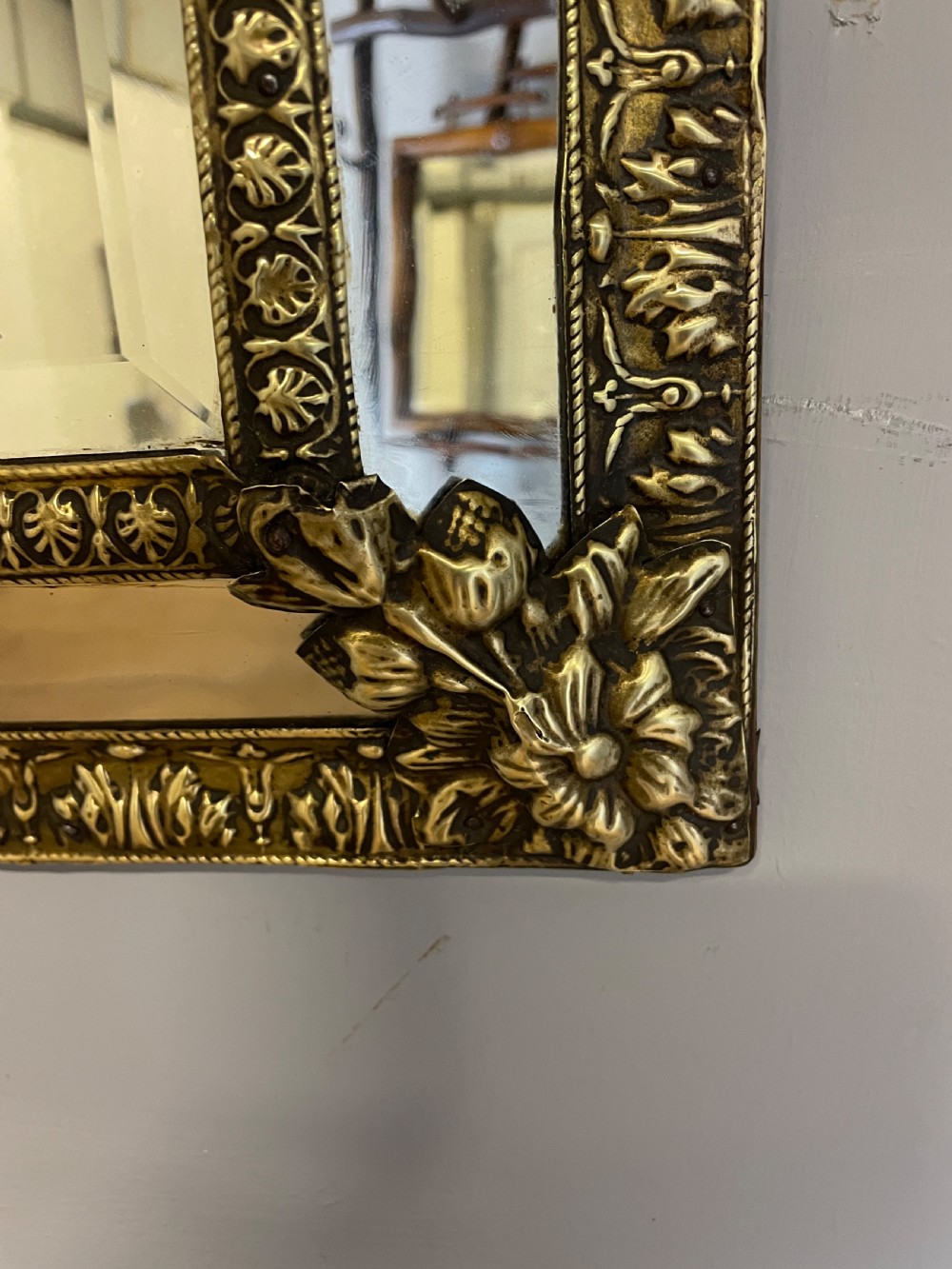 A nineteenth-century French cushion mirror featuring an ornate repousse brass frame with foliate cresting and bevelled mirror plates. View V