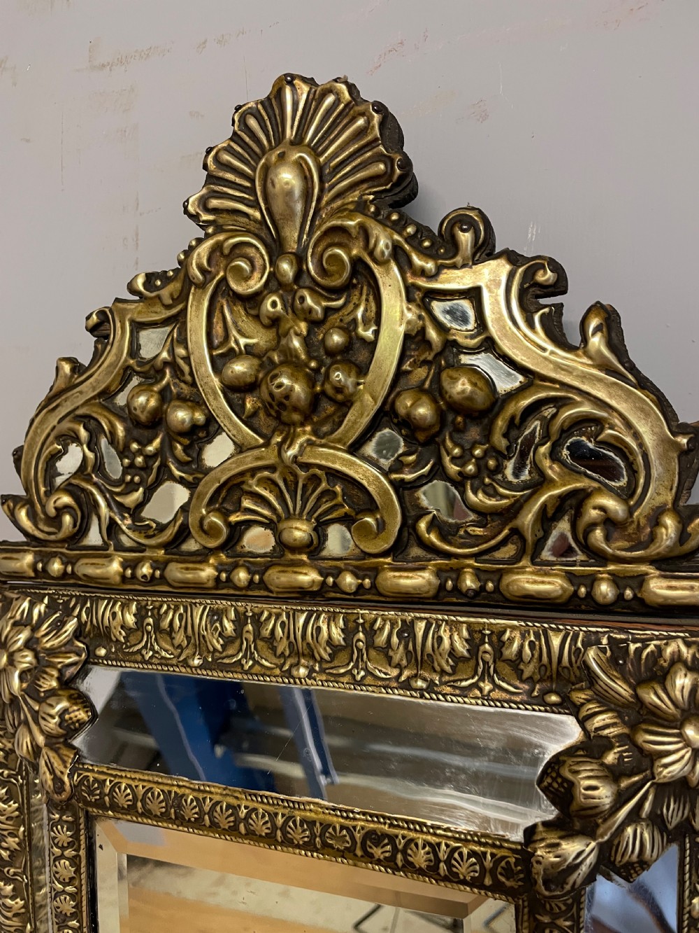 A nineteenth-century French cushion mirror featuring an ornate repousse brass frame with foliate cresting and bevelled mirror plates. View VI