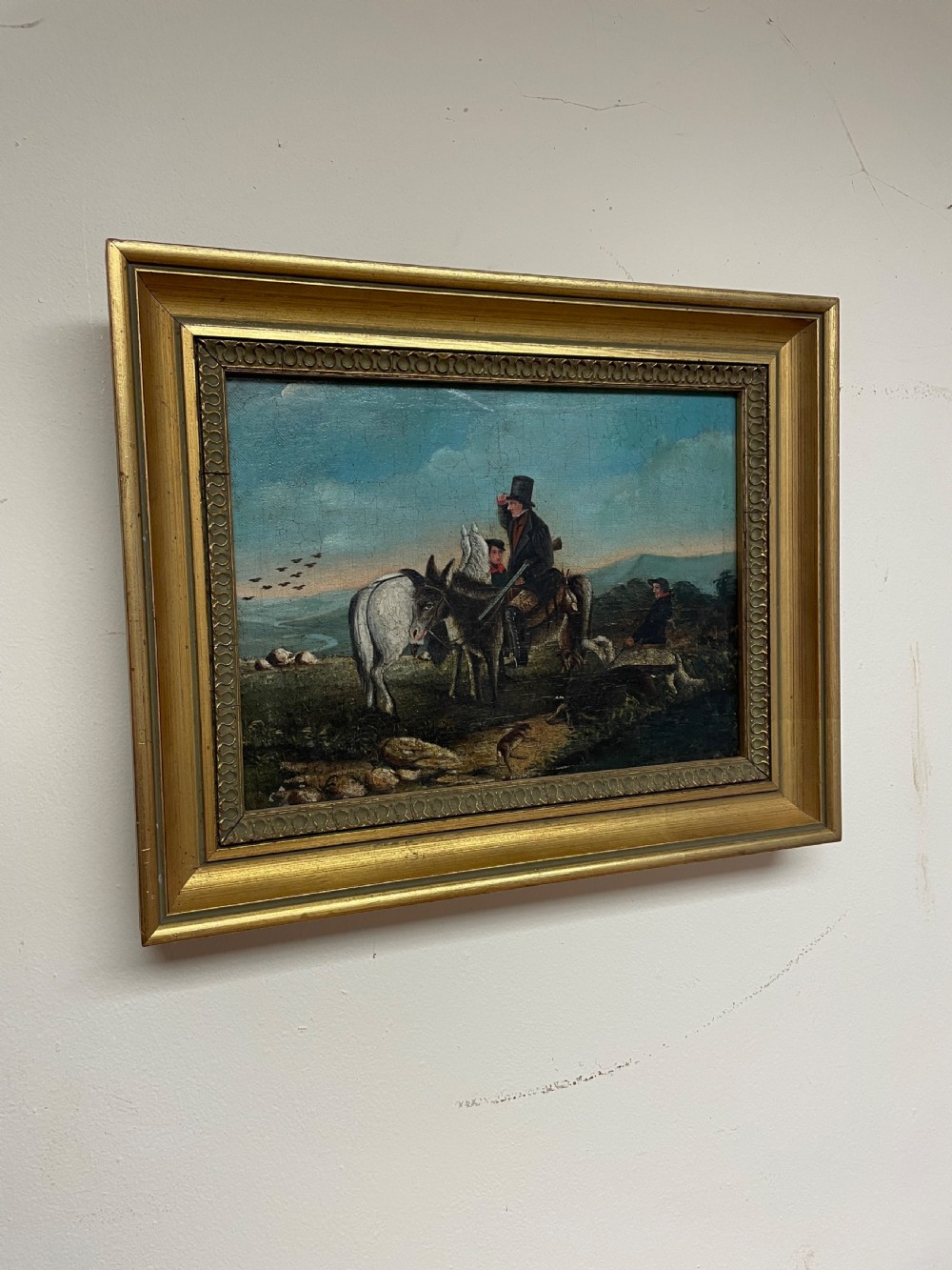 A 19th-century oil painting on canvas depicting riders and dogs in a rural landscape set within a moulded gilt frame.