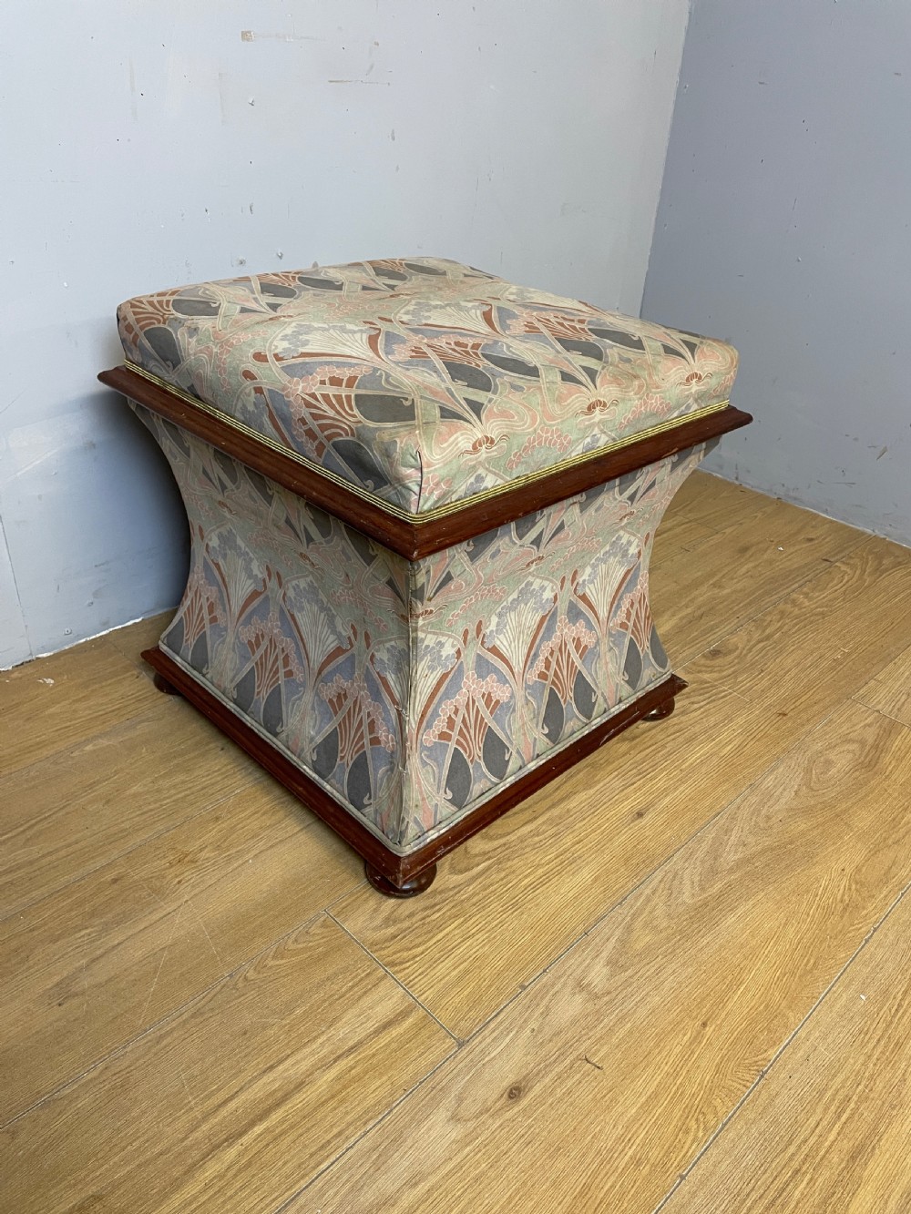 A nineteenth-century square waisted ottoman stool upholstered in a floral Liberty fabric with dark mahogany trim and bun feet.