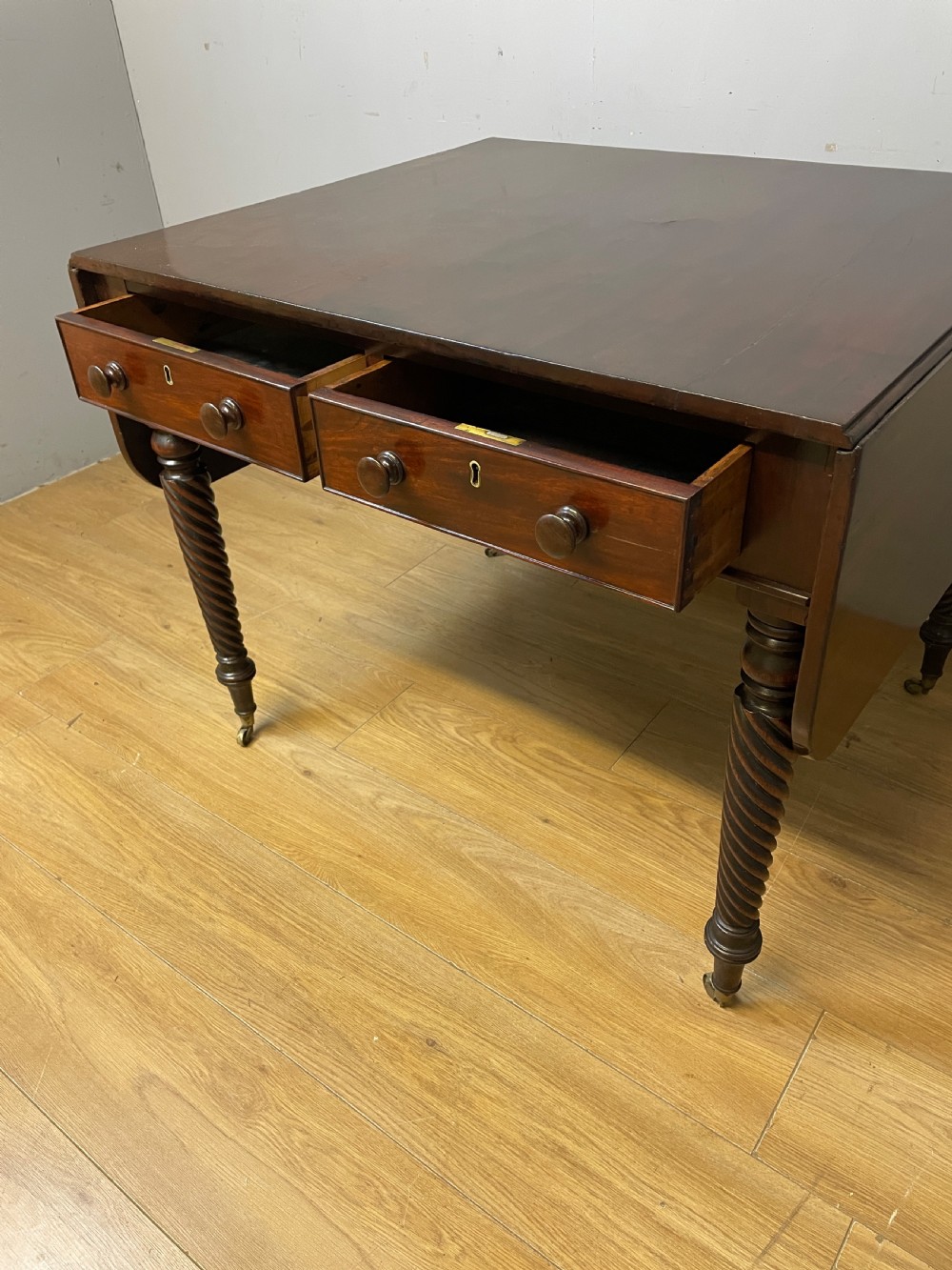 A dark mahogany Regency writing table featuring two drawers with wooden knobs, drop-leaf sides, and spiral-twisted legs on brass castors. View III
