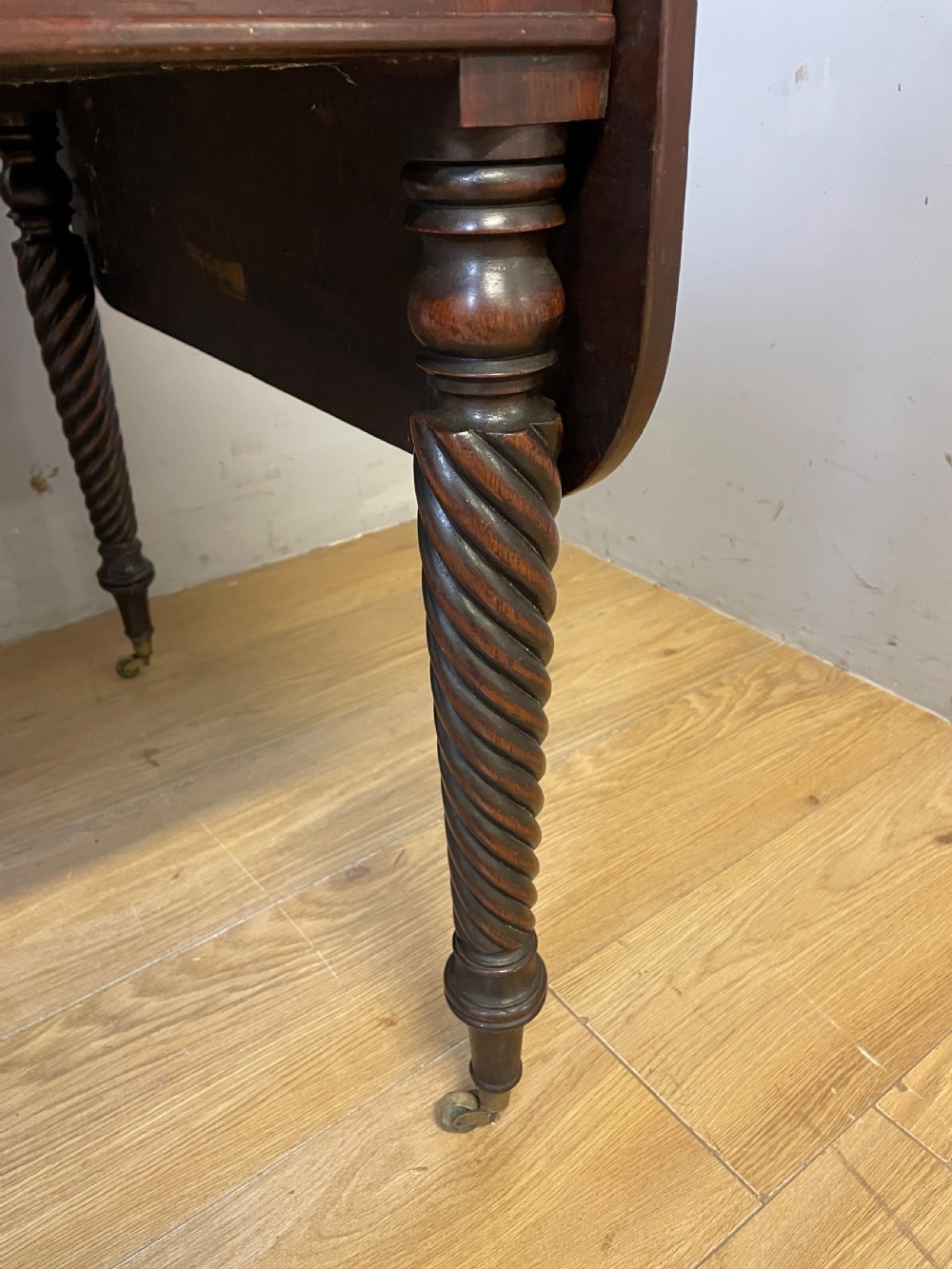 A dark mahogany Regency writing table featuring two drawers with wooden knobs, drop-leaf sides, and spiral-twisted legs on brass castors. View V