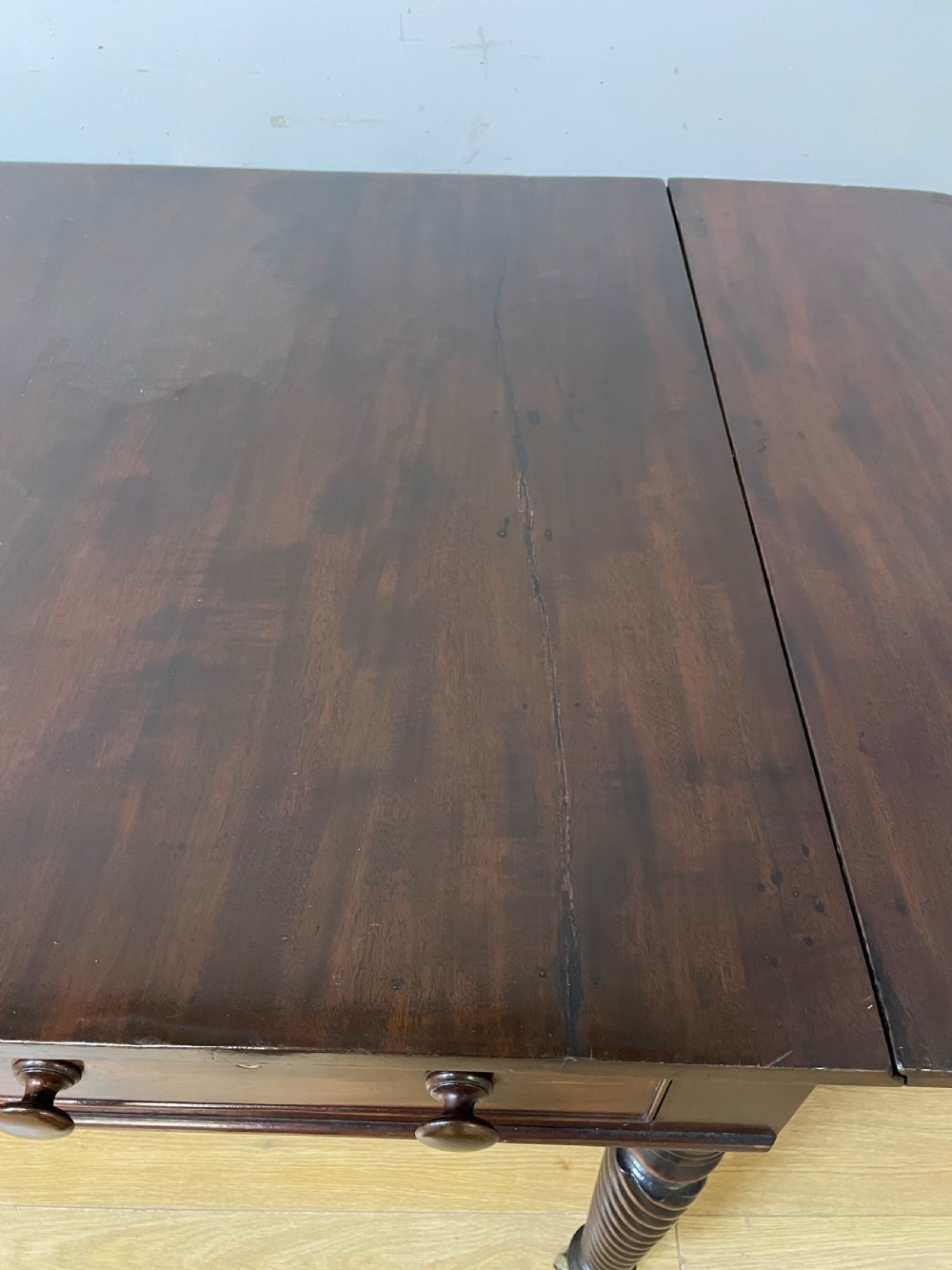 A dark mahogany Regency writing table featuring two drawers with wooden knobs, drop-leaf sides, and spiral-twisted legs on brass castors. View IX